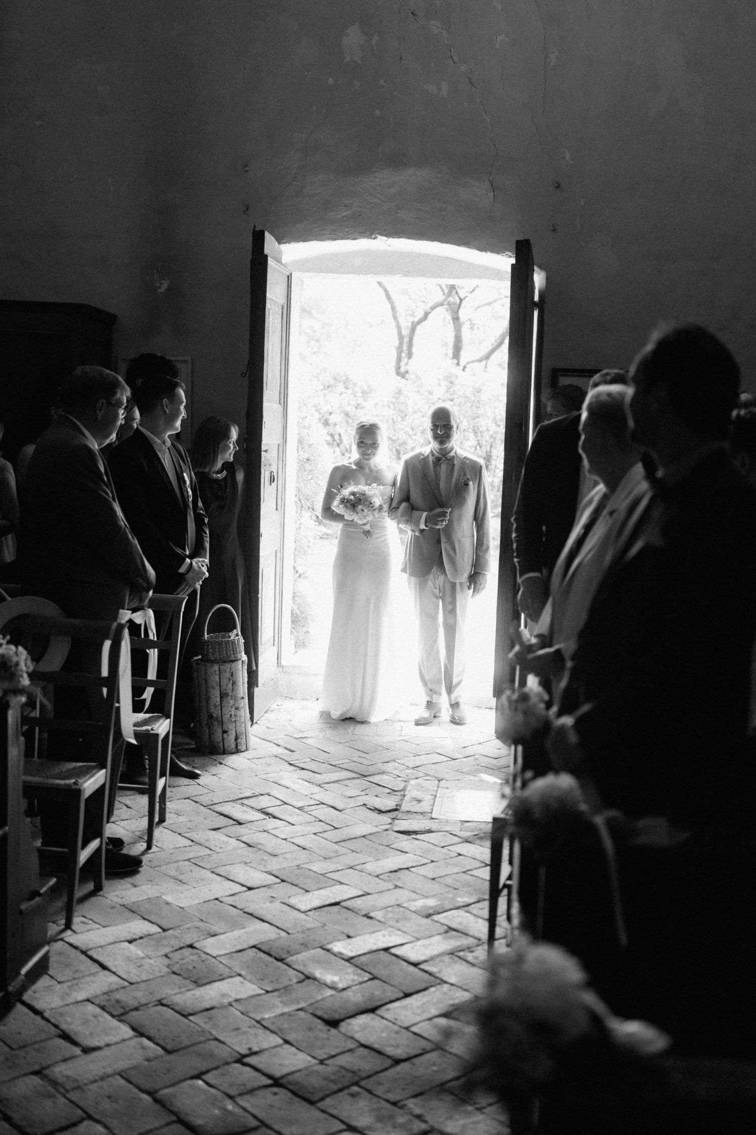 Black and white photo of a bride and groom silhouetted in a rustic church doorway during their wedding ceremony.