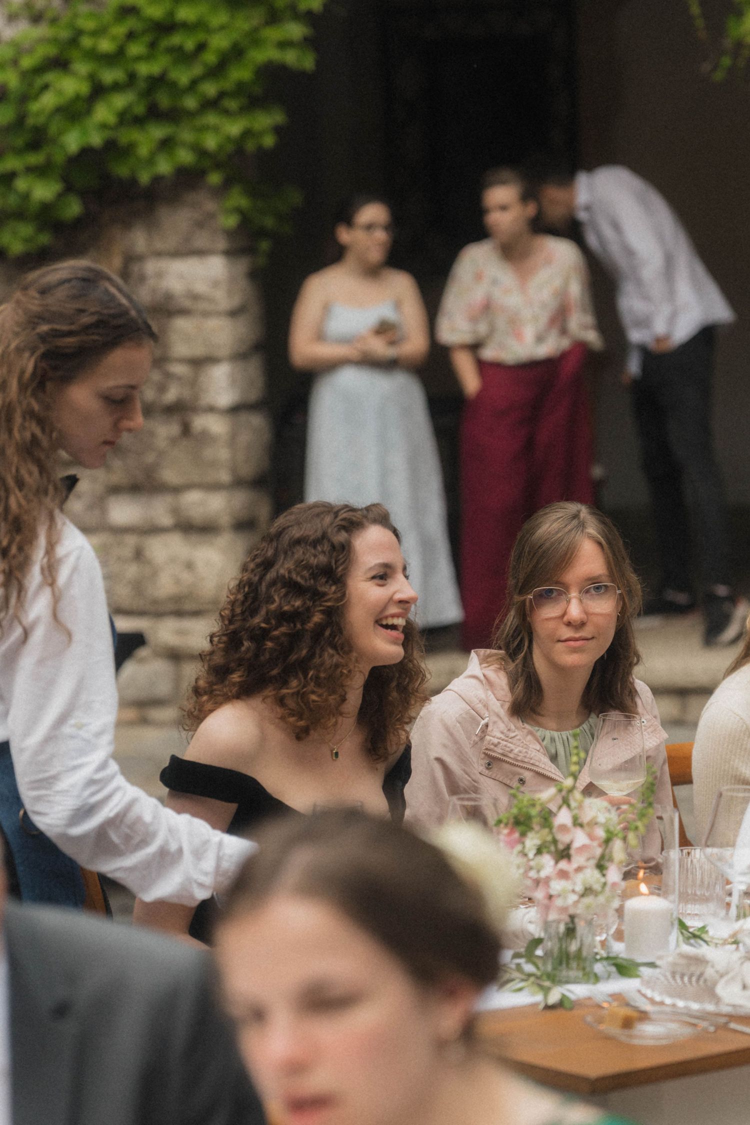 Wedding guests laughing and enjoying outdoor garden reception dinner at rustic venue.