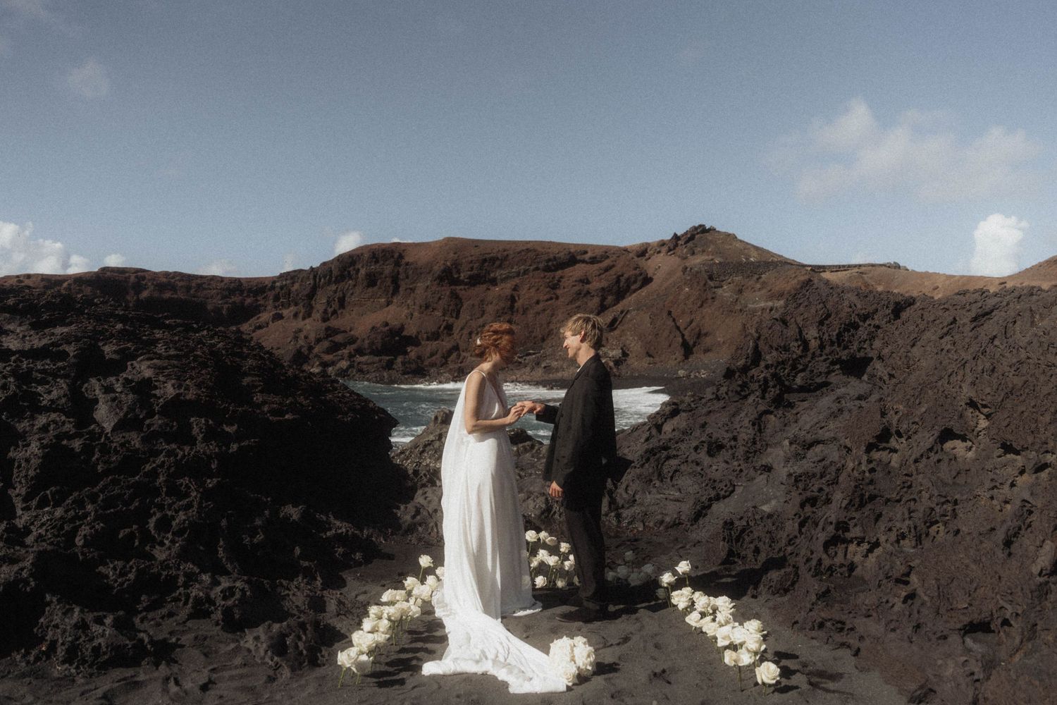Bride and groom exchanging vows on black sand beach surrounded by dramatic volcanic rock formations.