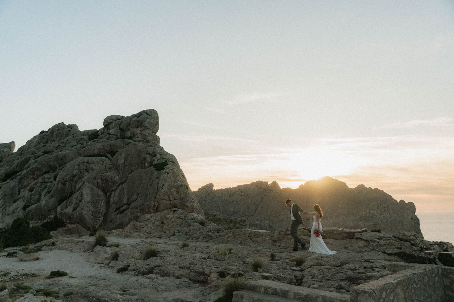 Bride and groom stand among rocky coastal cliffs at golden sunset during their outdoor elopement ceremony.
