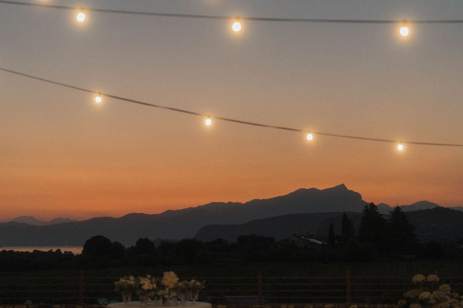 String lights glow against a stunning mountain sunset sky at an outdoor wedding reception.