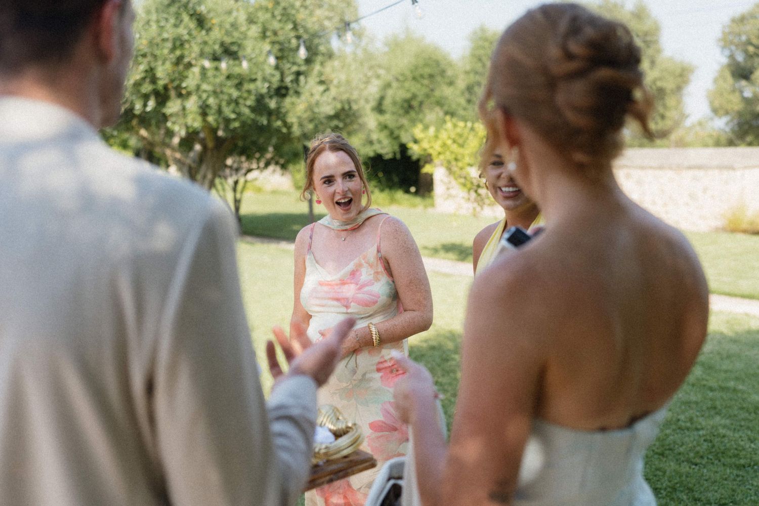 Guests laughing and celebrating outdoors at a sunny wedding reception in a lush green garden setting.