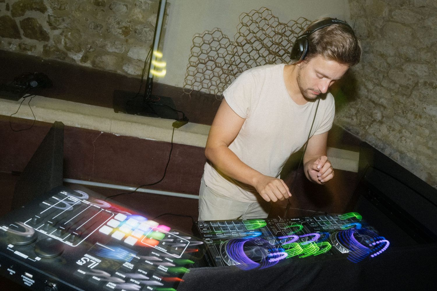 A DJ wearing headphones mixing music on a colorful illuminated DJ controller at a nightclub event.