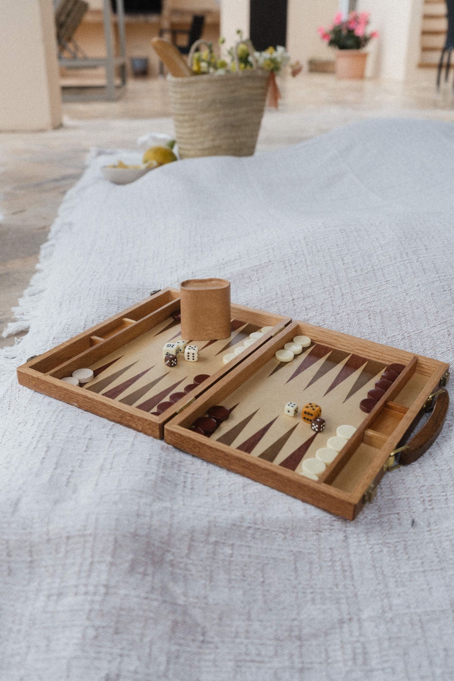 Wooden backgammon board game set up with dice and checkers on a light linen blanket outdoors.
