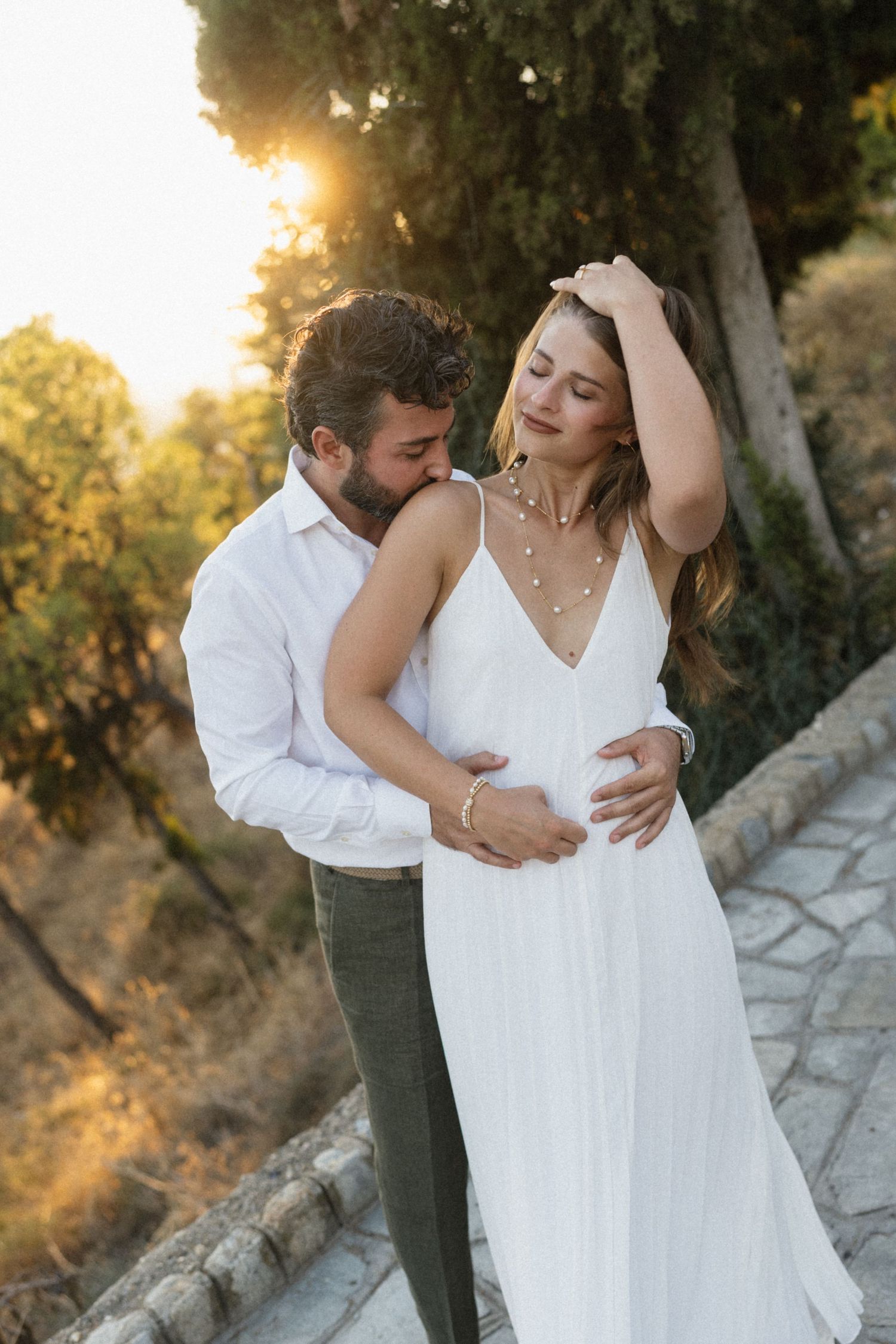 Bride and groom sharing a romantic golden hour moment outdoors, she in a white slip dress, he in a white shirt.