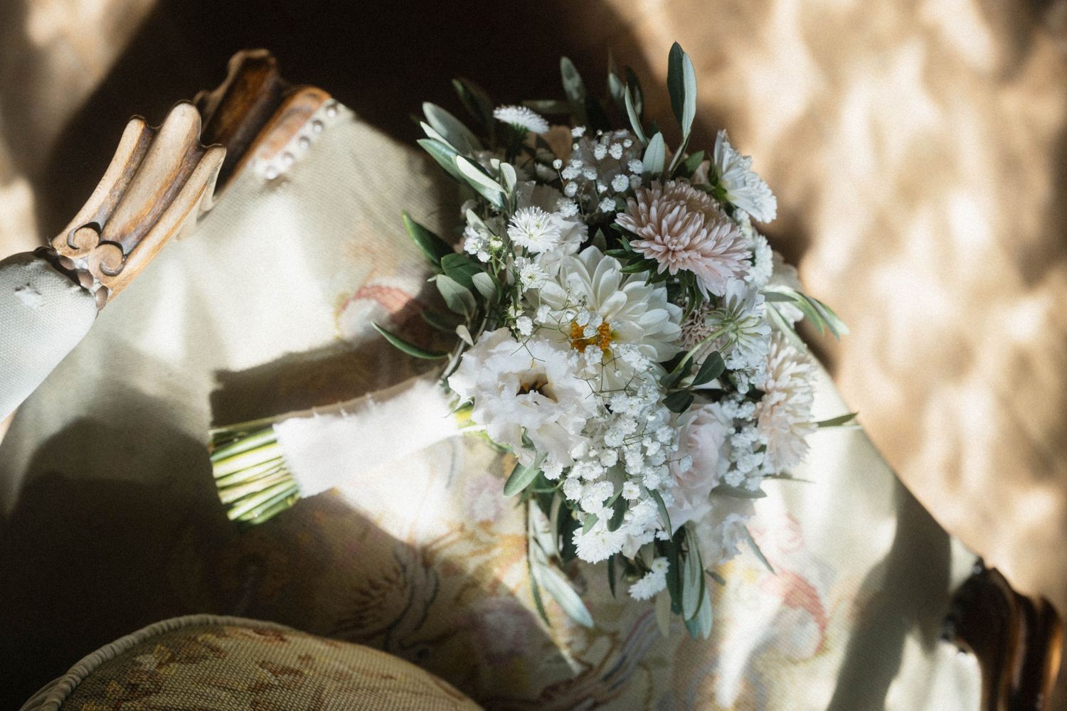 Bride holding a beautiful white and pink wedding bouquet with dahlias, baby's breath, and greenery in soft natural light.