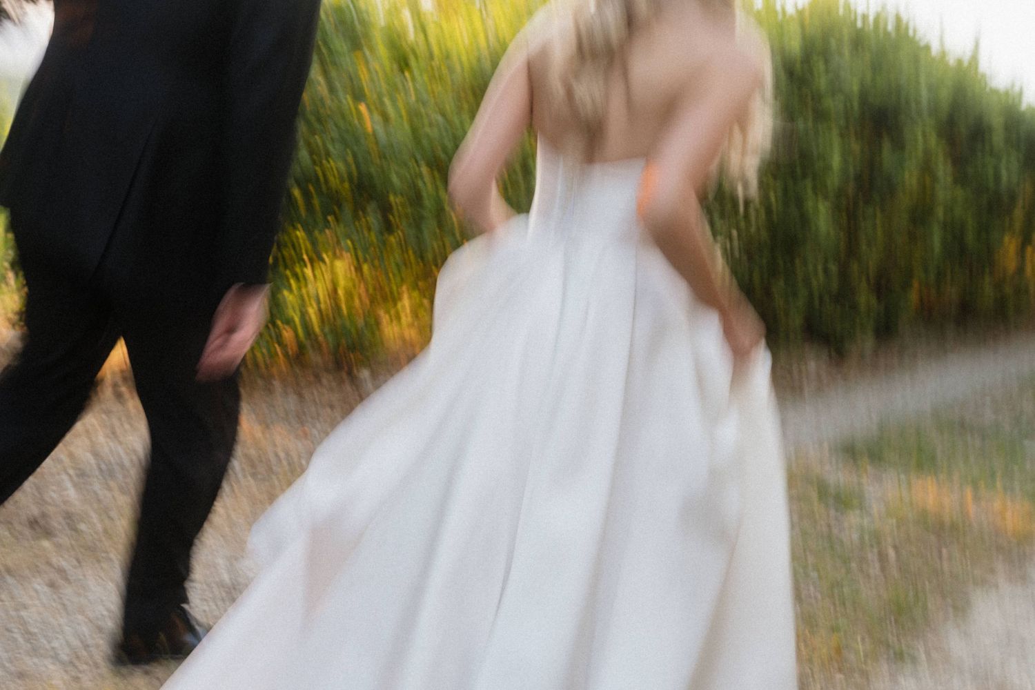Motion blur photo of a bride in a white gown and groom walking together outdoors.