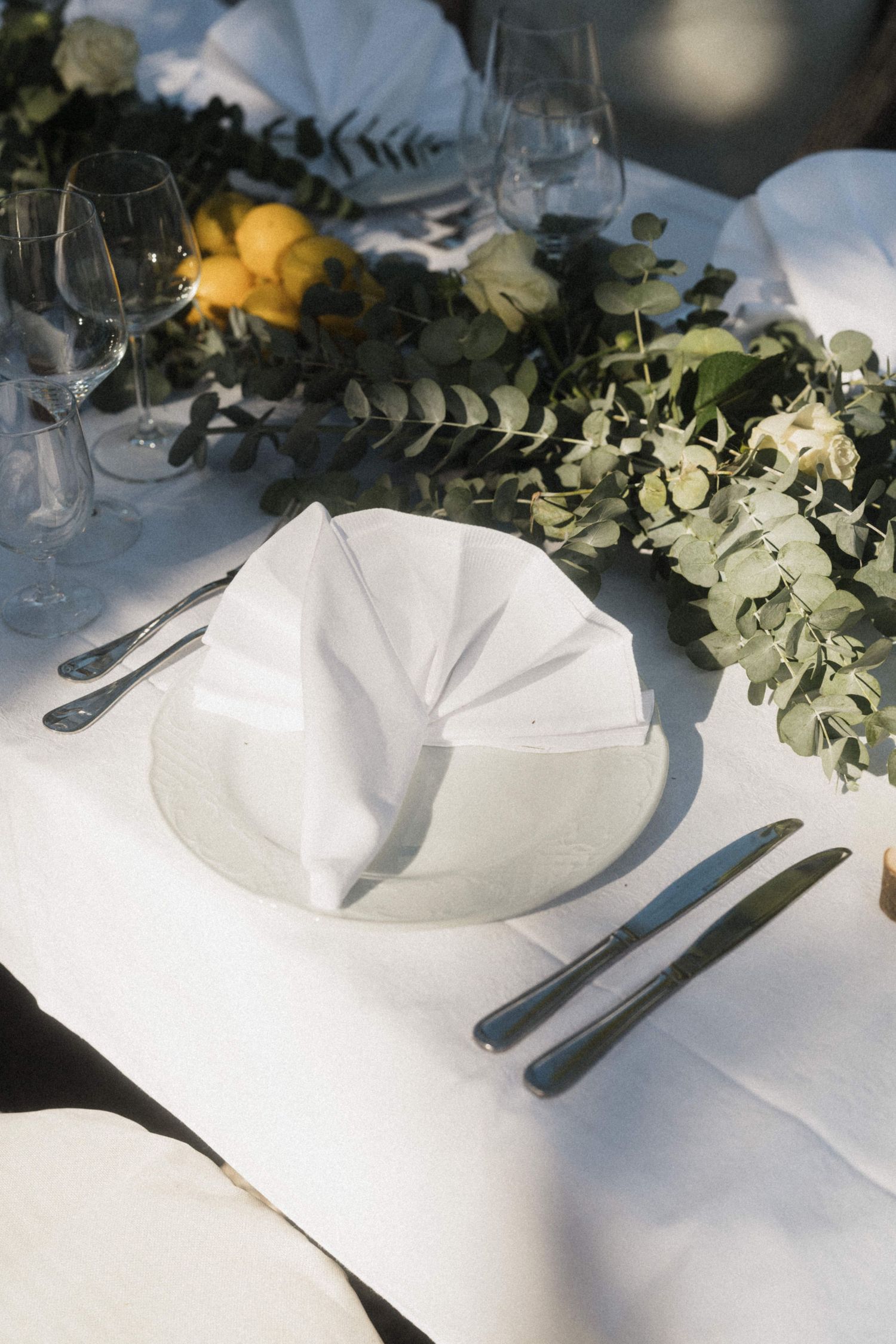 Elegant wedding table setting with folded white napkin, eucalyptus greenery, and fresh lemons.