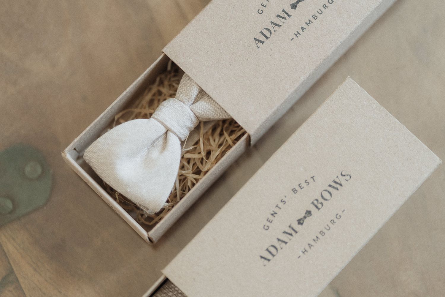 Adam Bows gents bow tie in white displayed in a kraft gift box with straw packaging.