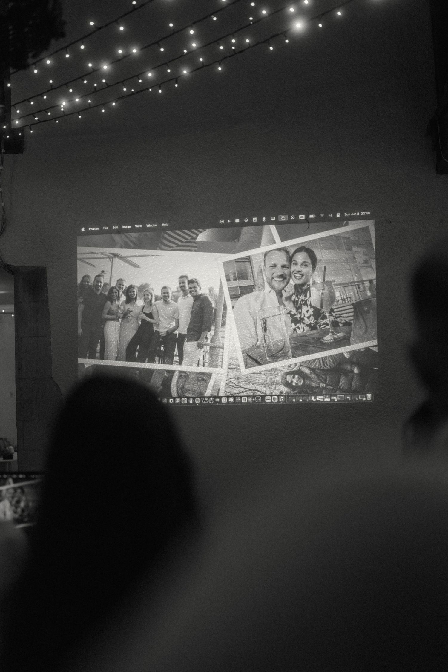 Black and white slideshow projection of couple photos at a wedding reception under string lights.