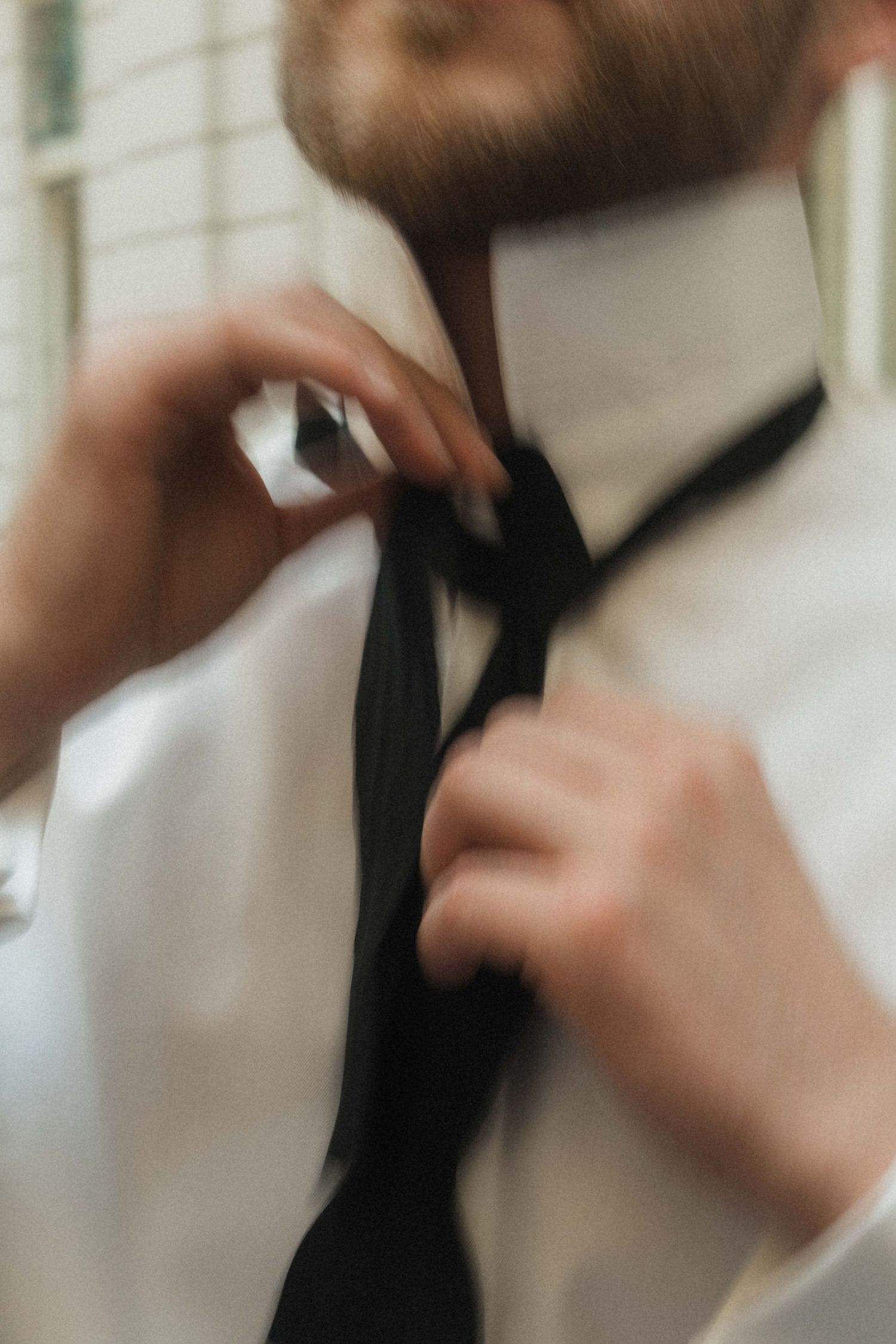 Close-up blurred shot of a groom tying a black necktie over a white dress shirt before his wedding.