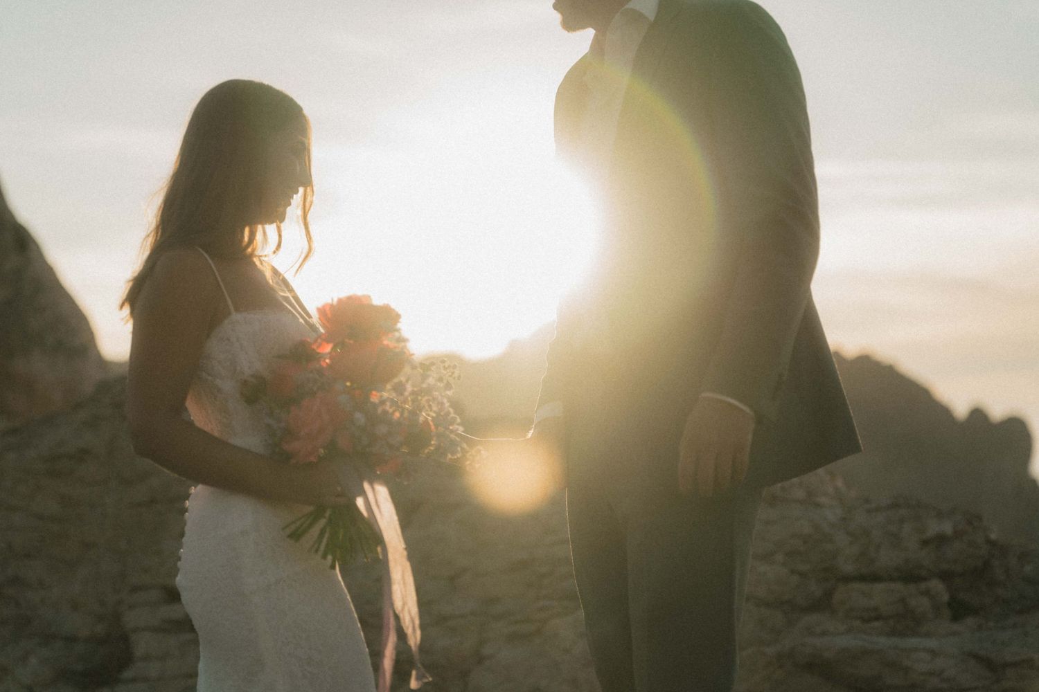 Bride and groom share a romantic sunset moment outdoors, bride holding a colorful bouquet during a scenic mountain elopement.