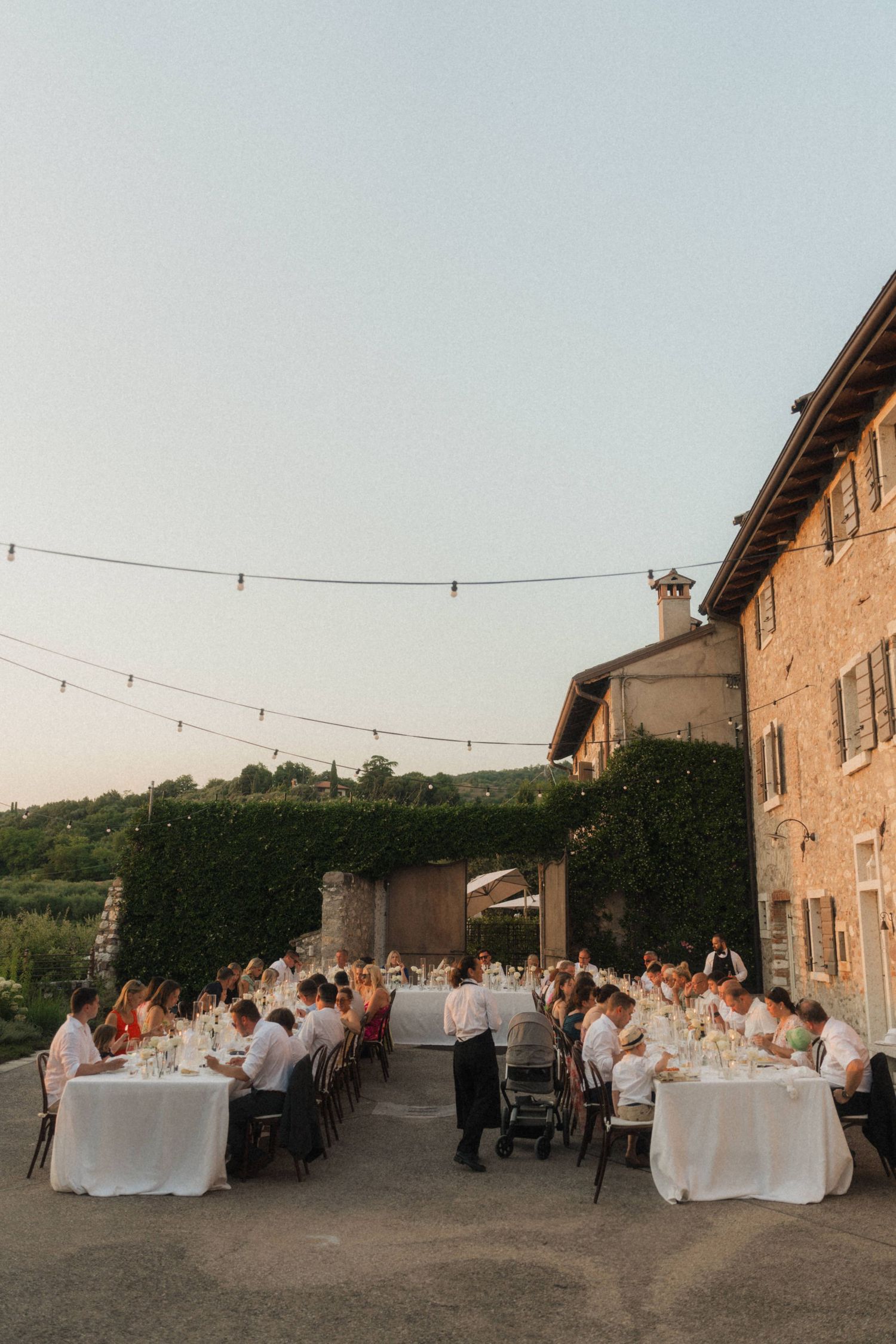Elegant outdoor wedding reception dinner at a rustic Italian stone estate with string lights at twilight.