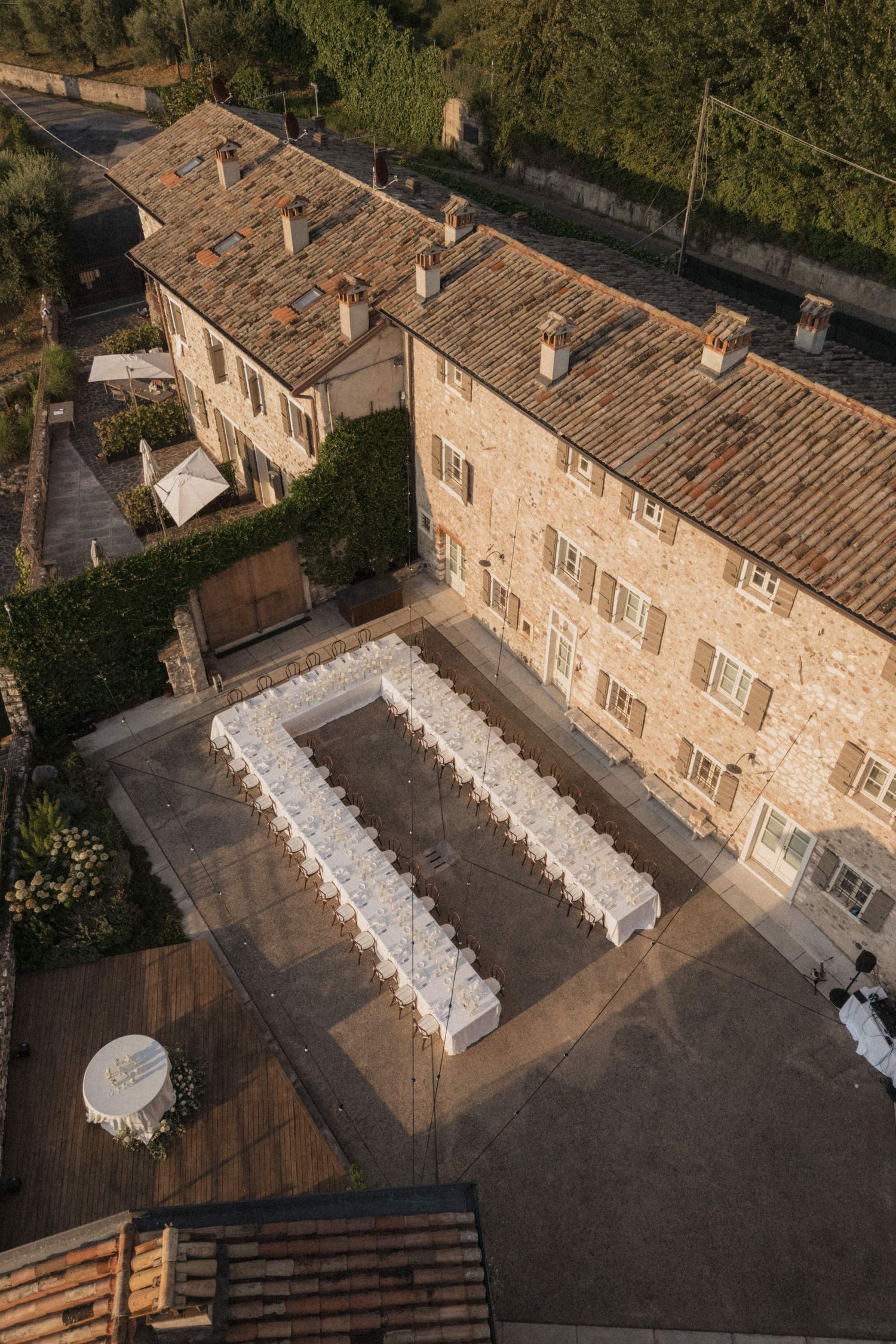 Aerial view of rustic Italian stone villa with elegant U-shaped wedding reception tables.