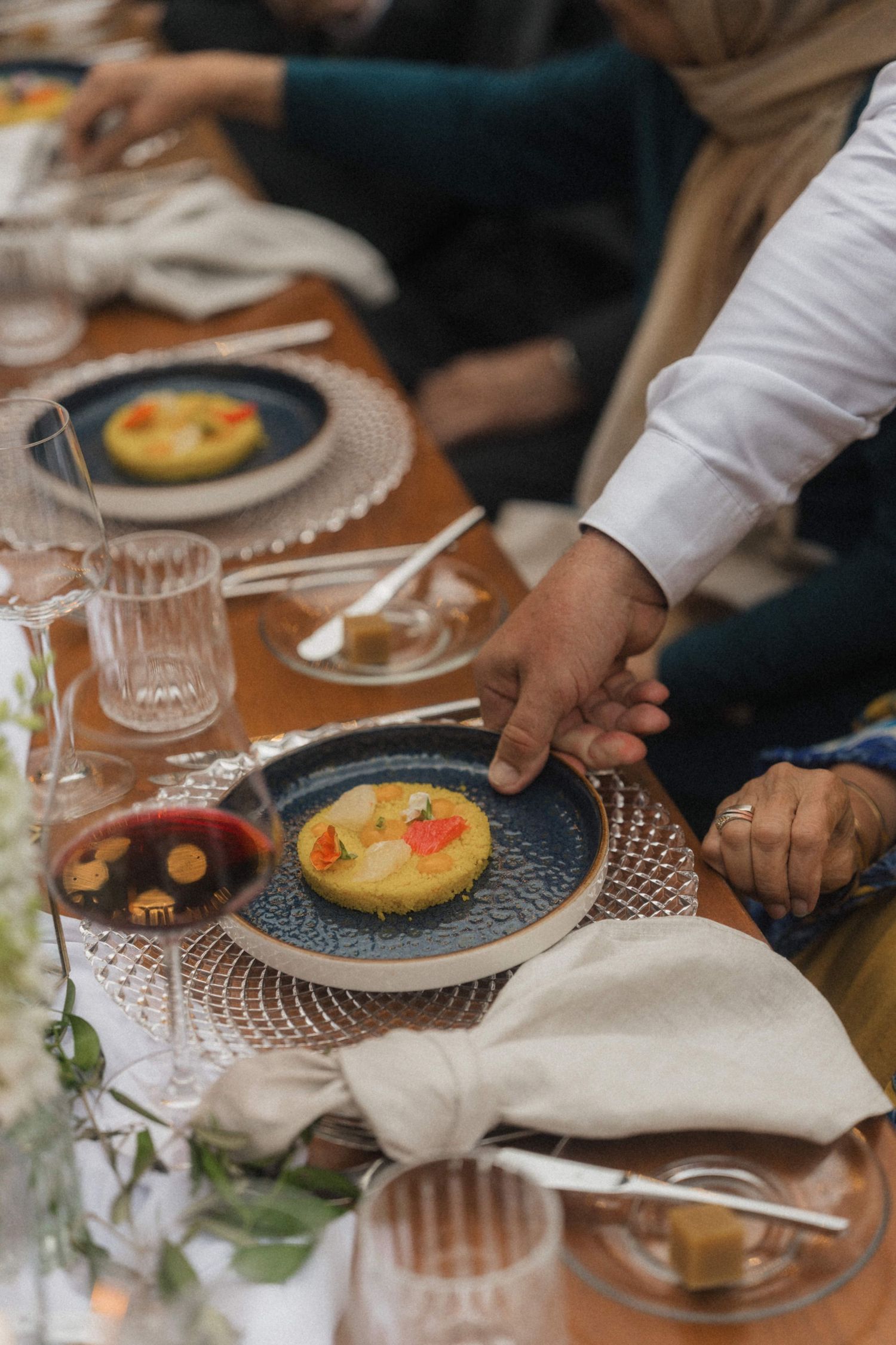 Server placing elegant plated dish on beautifully set wedding reception dinner table with glassware and floral decor.