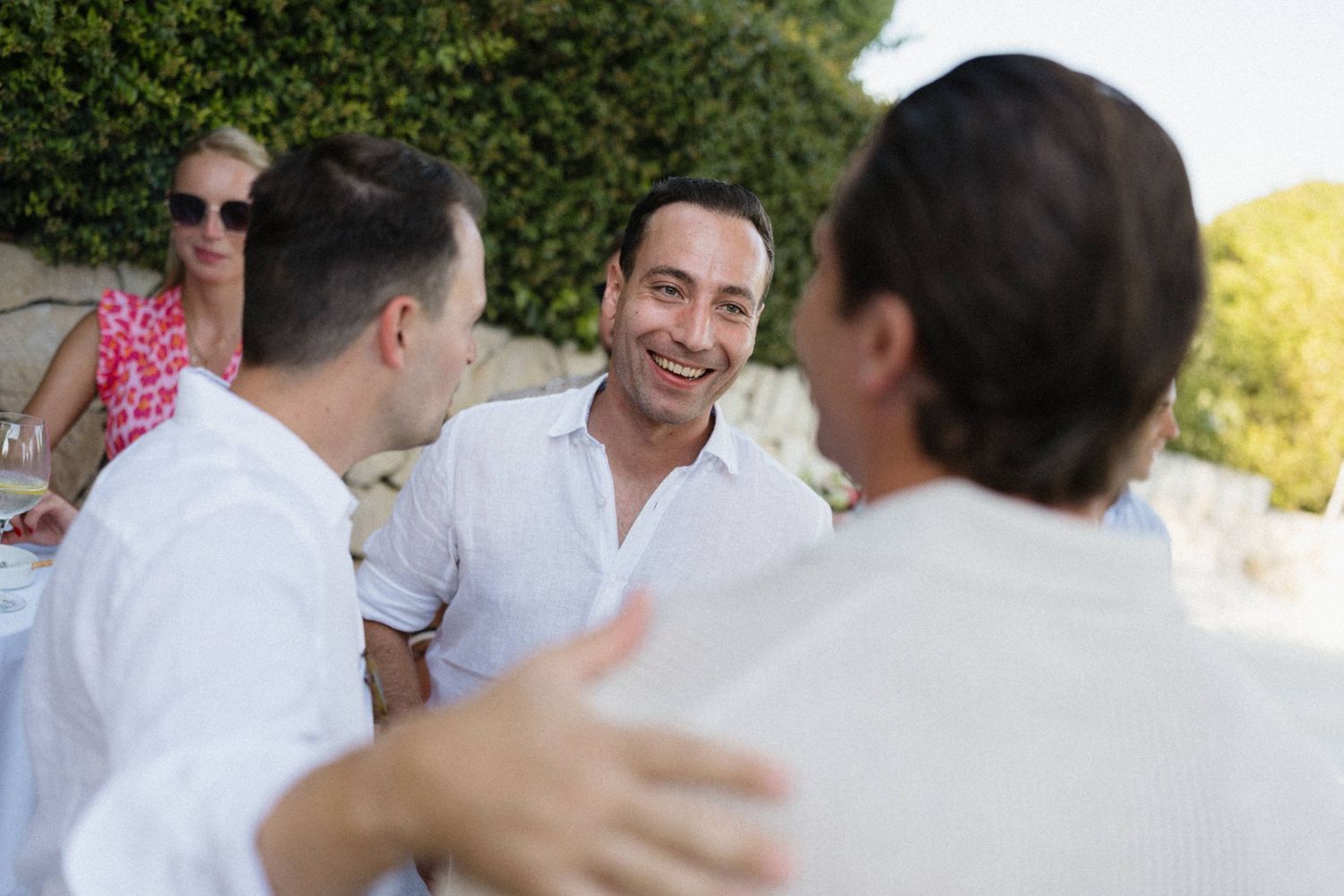 Group of people in white shirts socializing outdoors at a sunny garden party event.