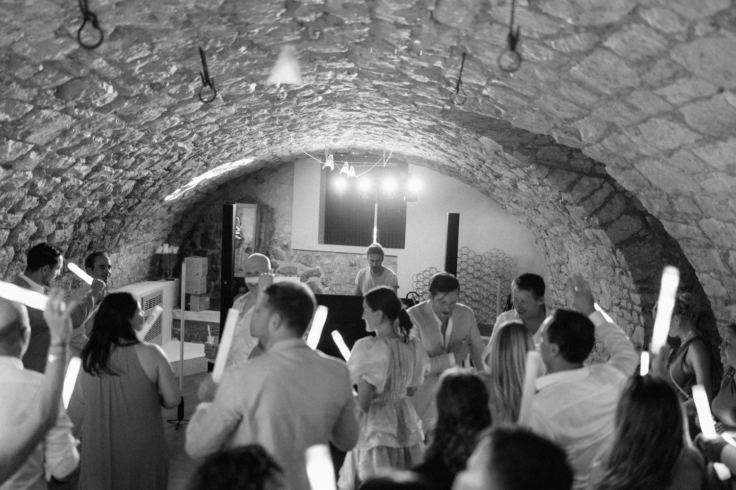Black and white photo of wedding guests dancing under a stone arched ceiling venue.