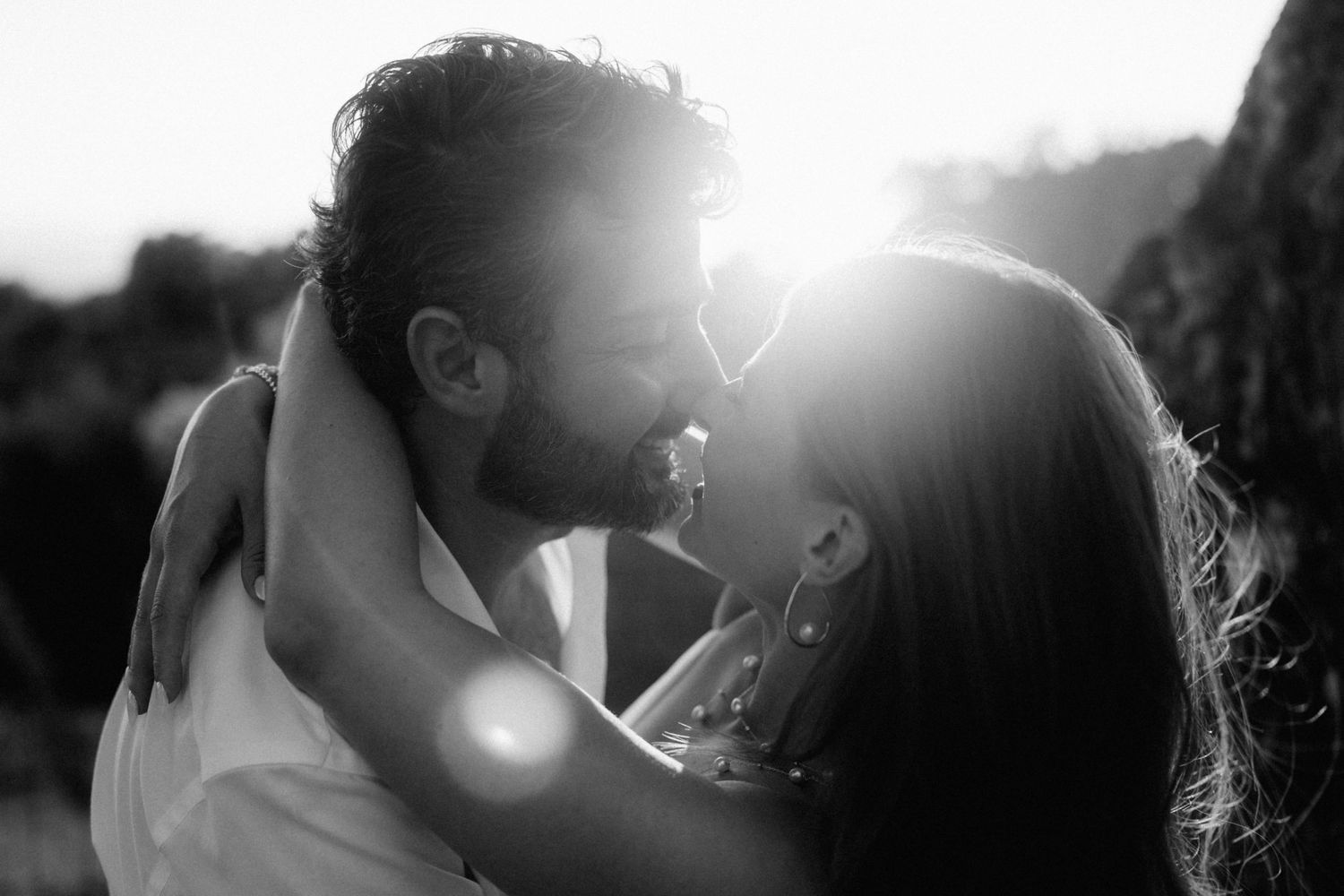 Black and white photo of a couple sharing a romantic moment, backlit by golden sunlight at sunset.