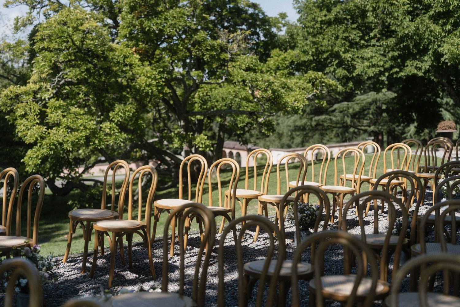Rows of elegant bentwood chairs arranged outdoors for a garden wedding ceremony surrounded by lush green trees.