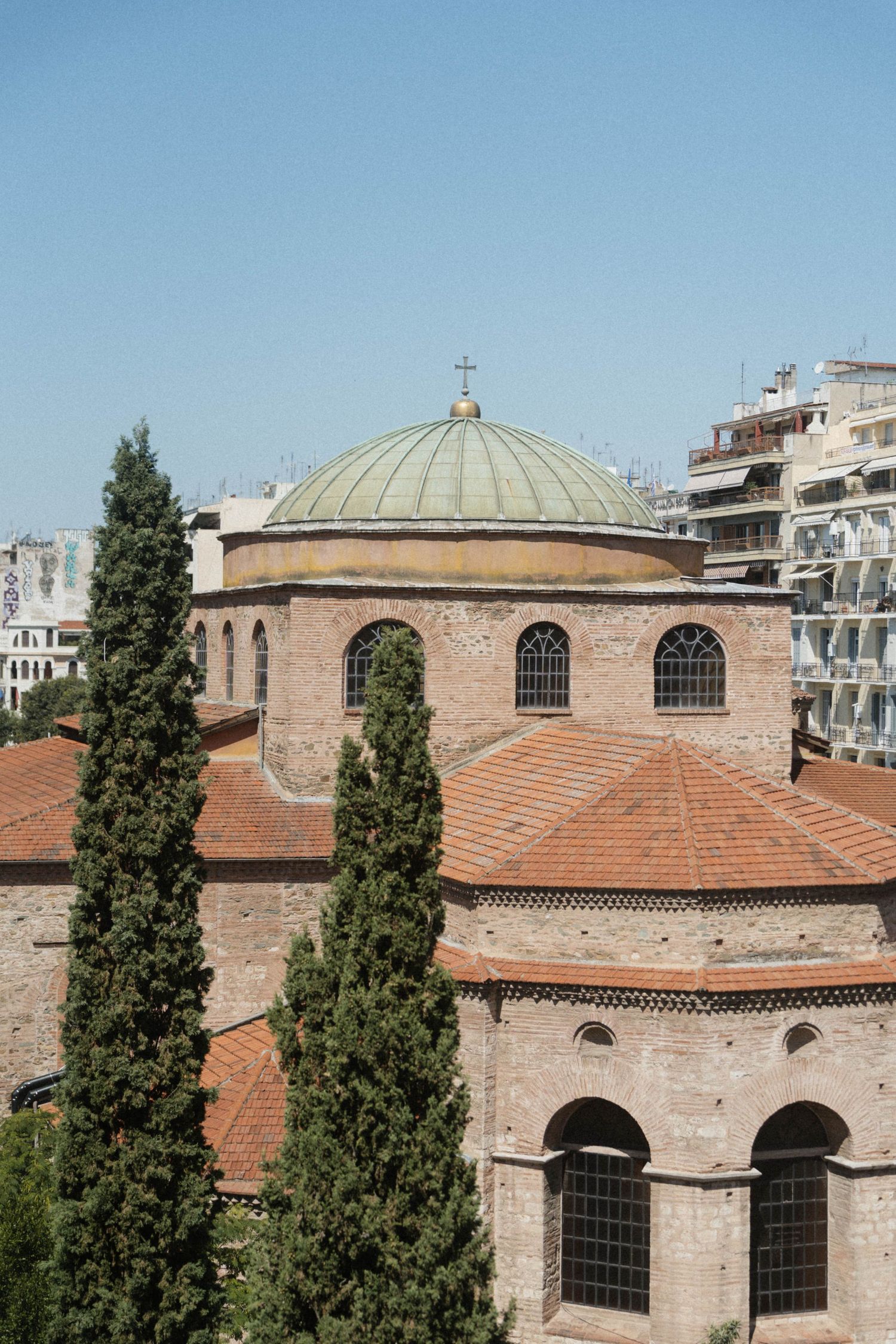 Ancient Byzantine church with green dome, red tile roof, and cypress trees in Thessaloniki, Greece.