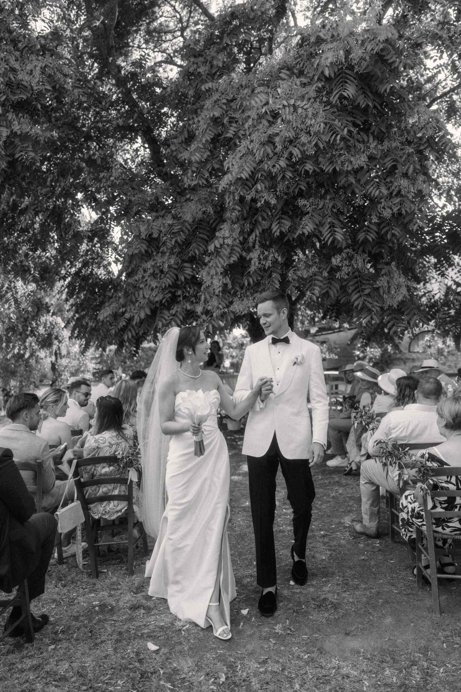 Black and white photo of bride and groom walking hand in hand after outdoor wedding ceremony.