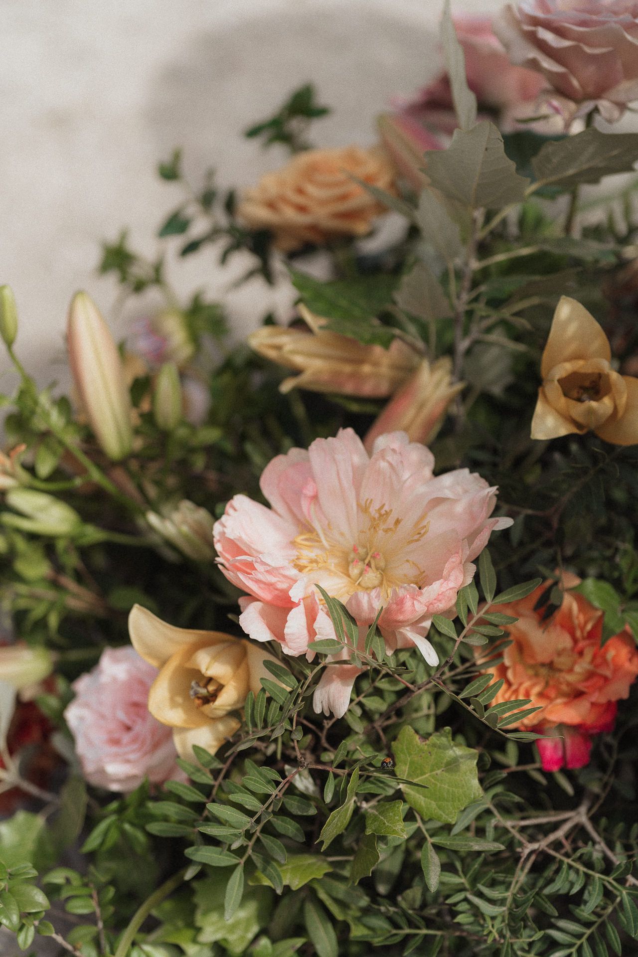 A lush floral arrangement featuring pink peonies, roses, and mixed blooms with green foliage in soft pastel tones.