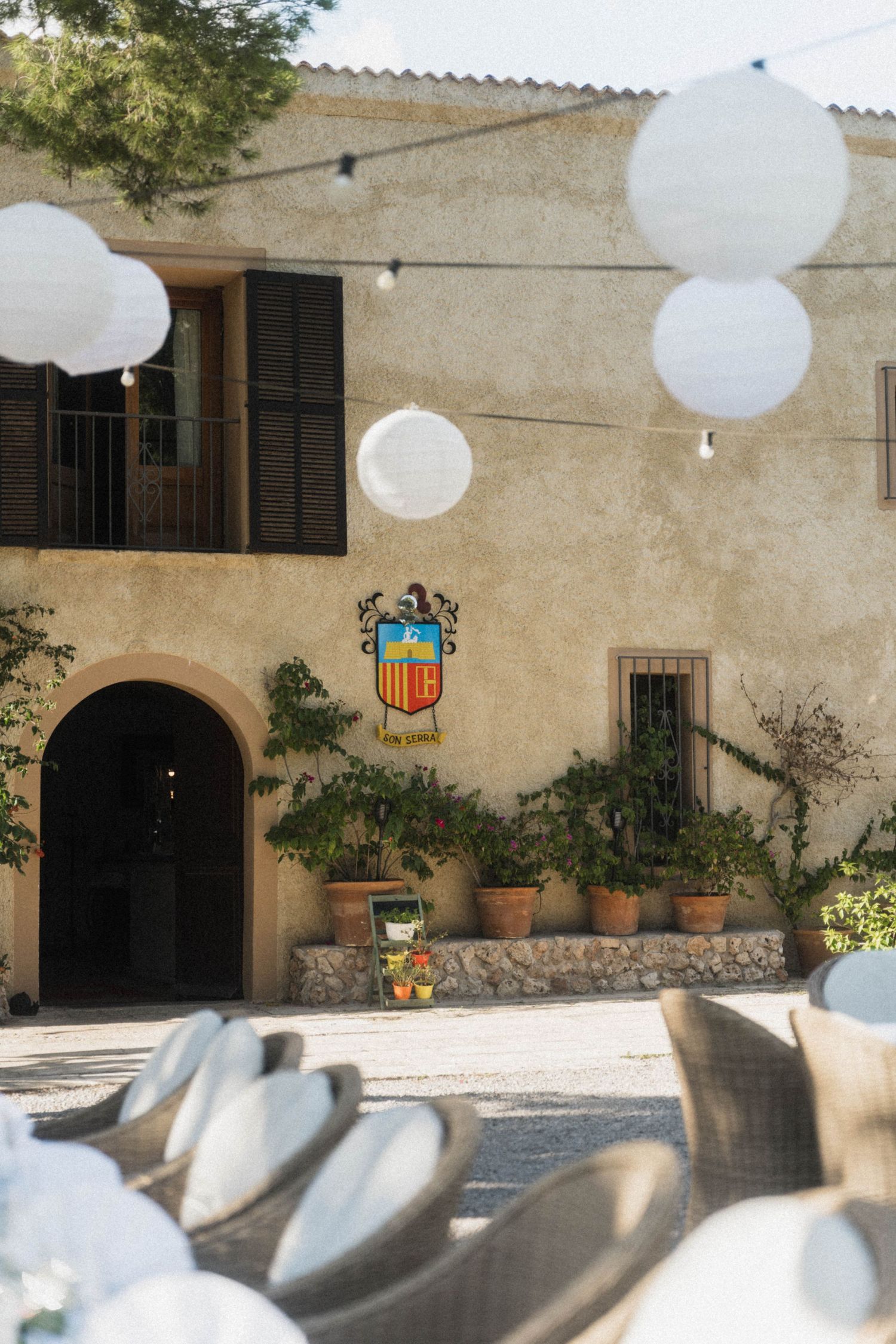 Rustic Mediterranean venue with coat of arms, white lanterns, and wicker chairs for outdoor wedding.