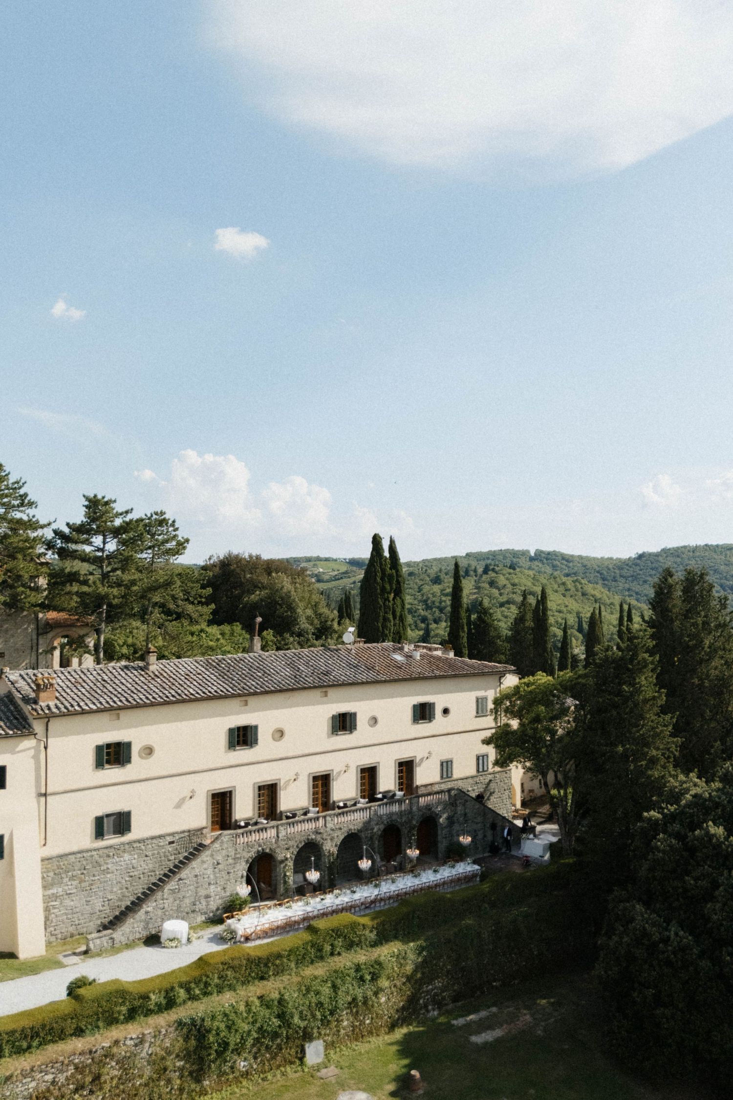 Aerial view of a historic Italian villa wedding venue surrounded by cypress trees and rolling Tuscan hills.