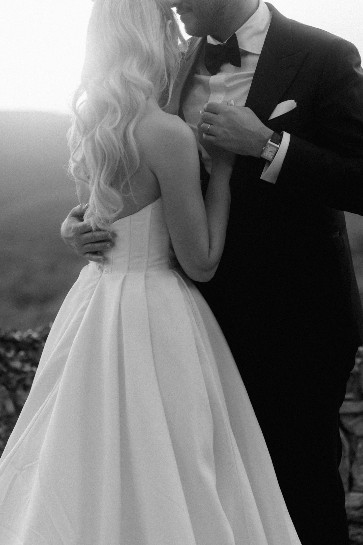 Black and white photo of a bride and groom embracing closely showing the brides elegant gown.