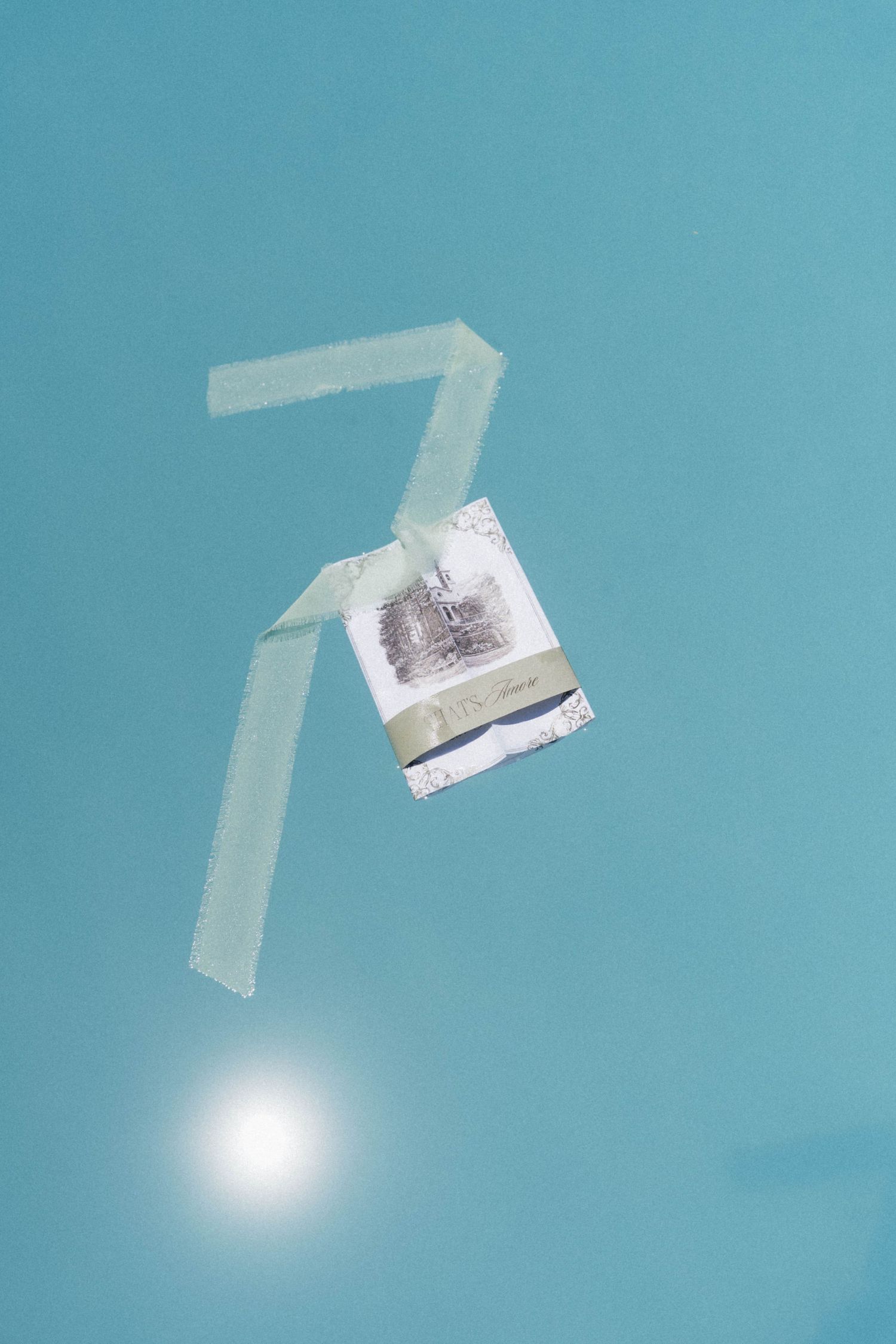 Wedding invitation card floating underwater with number seven visible against turquoise pool background.