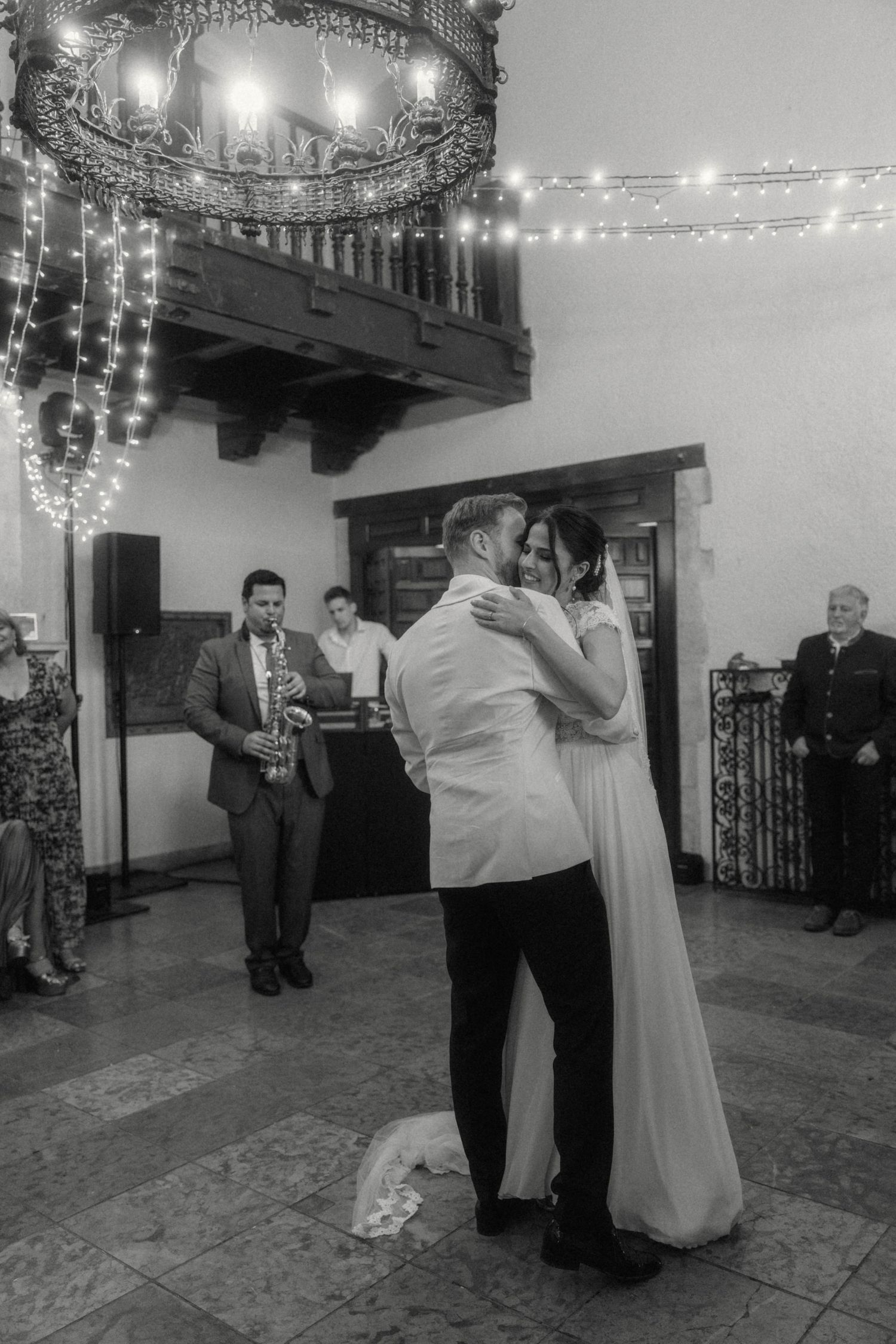Black and white photo of bride and groom sharing first dance with saxophonist performing.