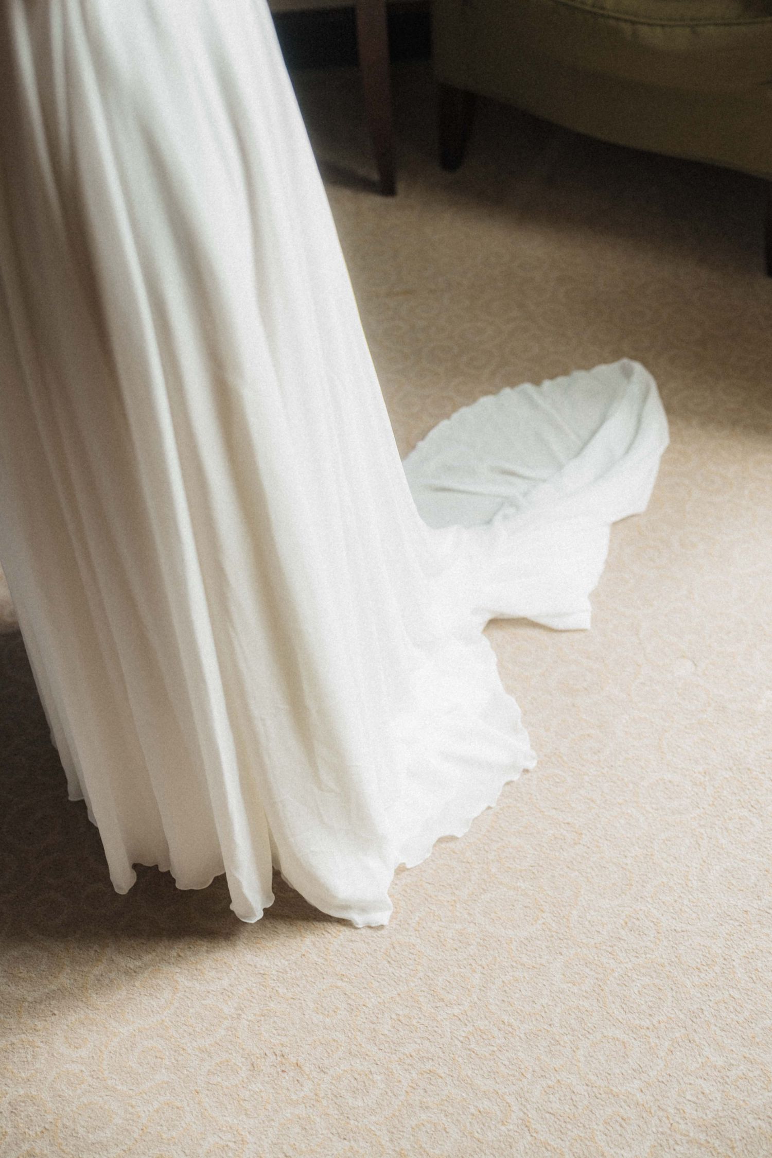Elegant white bridal gown with flowing train and delicate lace hem on beige carpet.