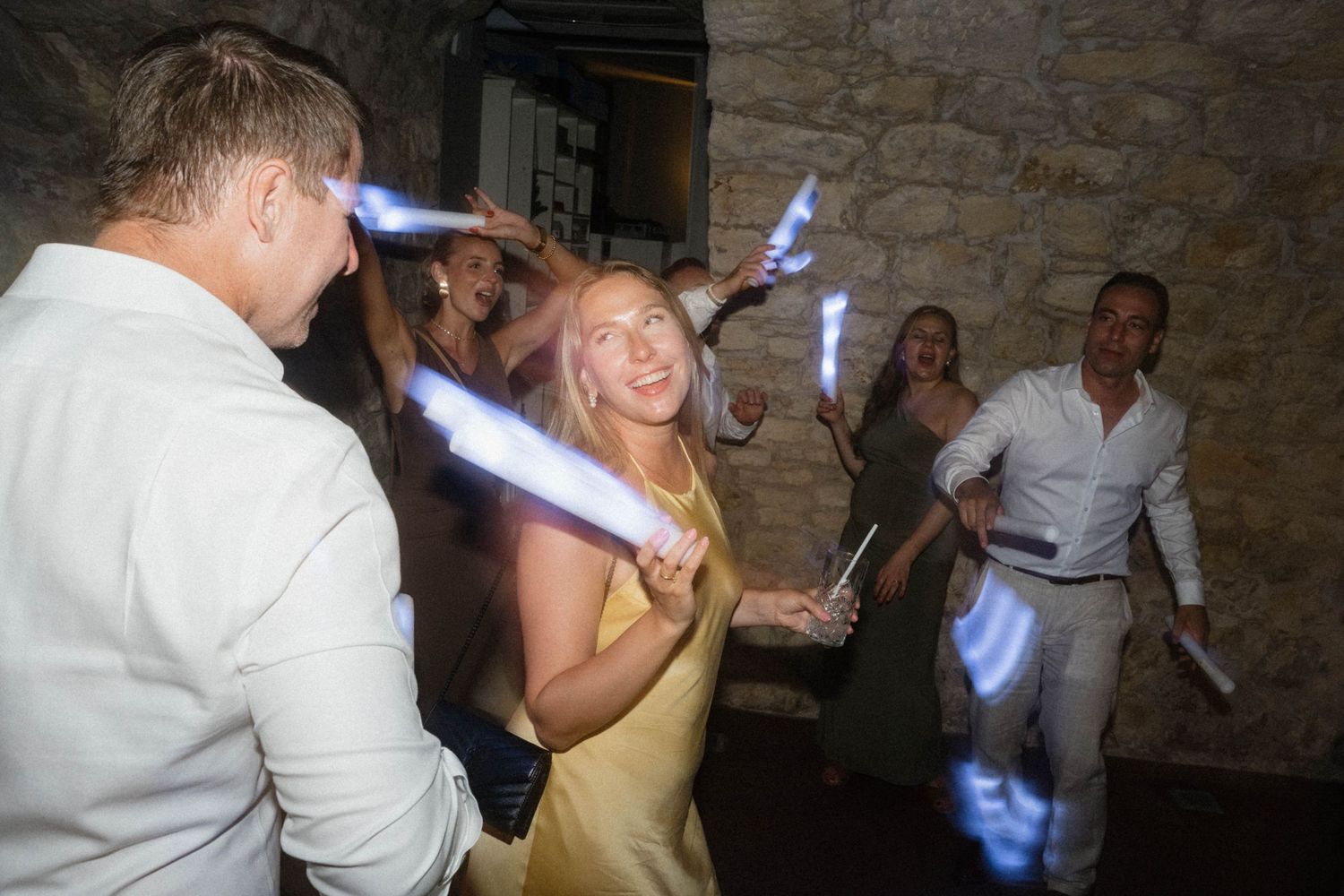 Guests dancing with glowing light sticks at a lively wedding reception party indoors.