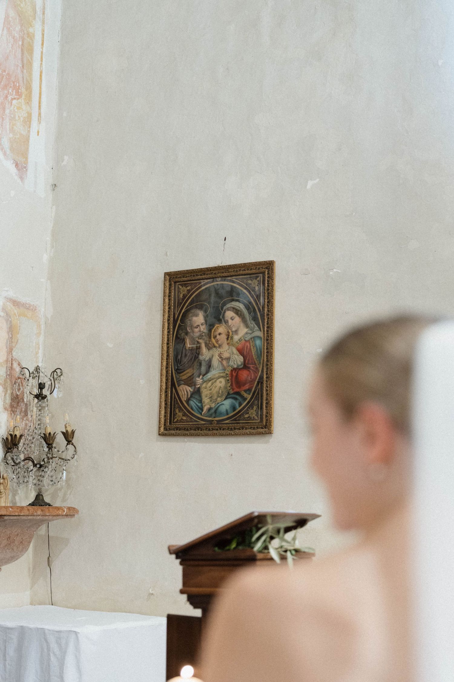 Religious painting of the Holy Family hangs on a rustic chapel wall during a wedding ceremony.