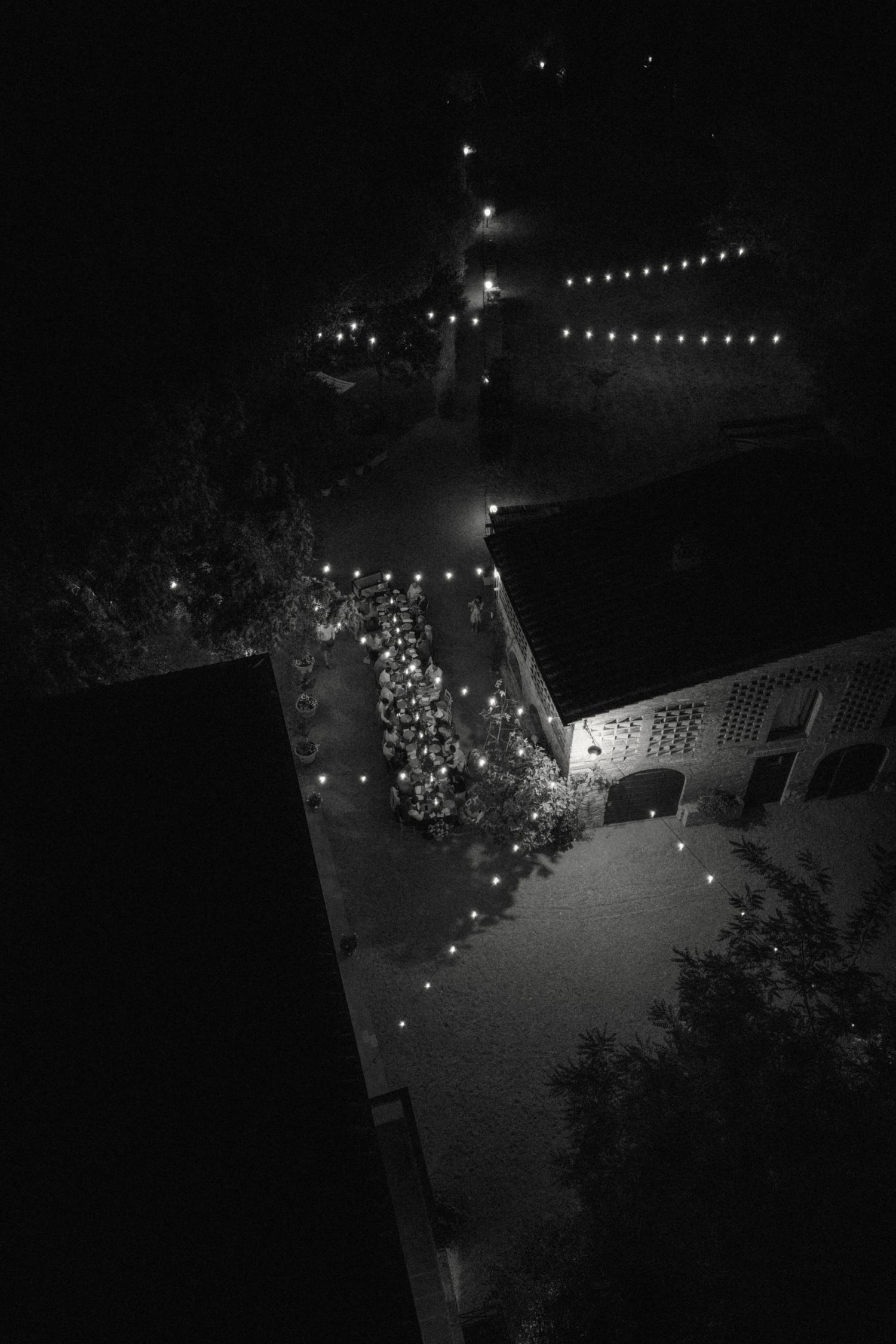 Aerial black and white night view of wedding venue illuminated by string lights.