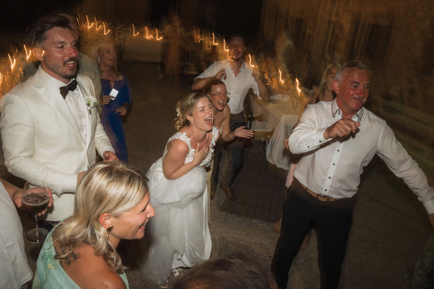 Joyful wedding reception celebration with bride, groom, and guests dancing with sparklers at an outdoor evening party.