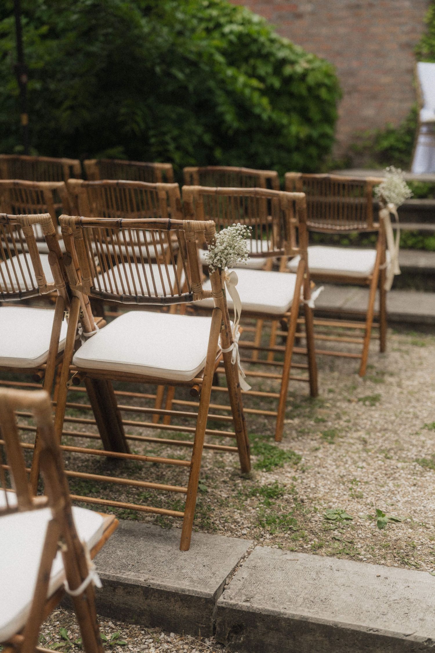Wooden folding chairs with white cushions and baby's breath floral accents arranged for an outdoor wedding ceremony.