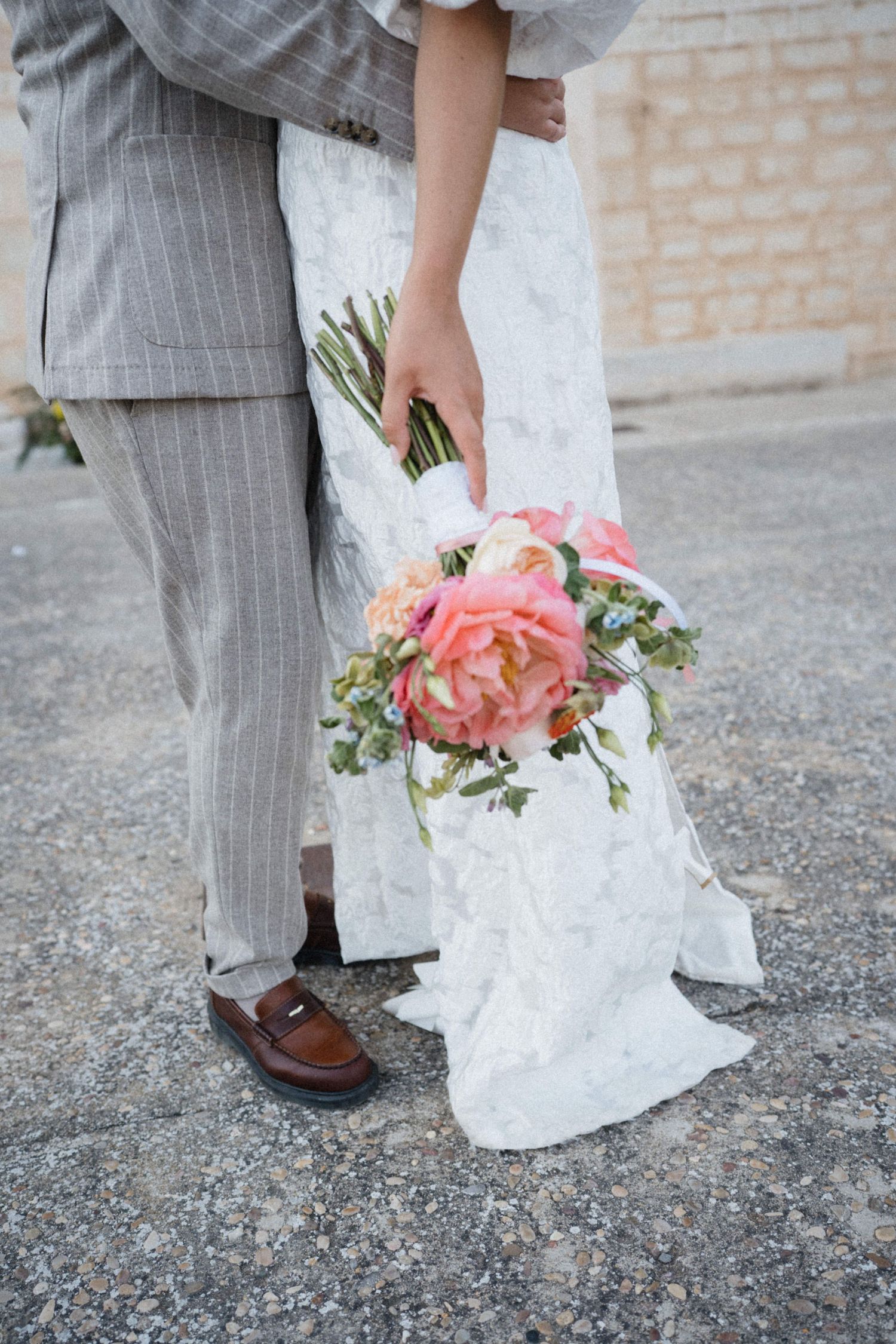 Close-up of bride and groom holding a pink peony bridal bouquet at outdoor wedding.