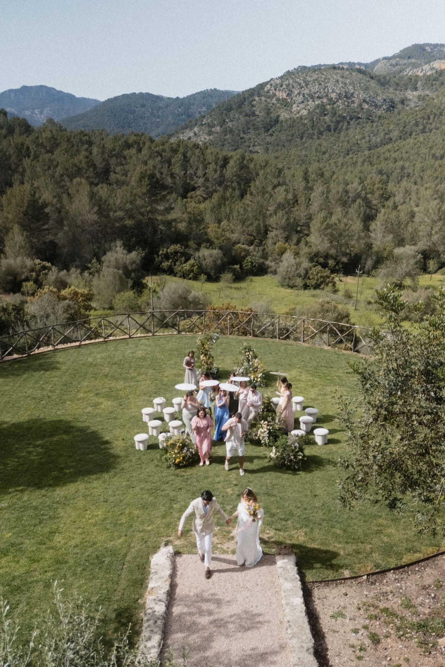 Aerial view of an outdoor wedding ceremony on a green lawn surrounded by mountains and forest in Mallorca.
