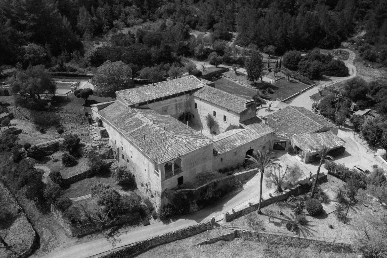Aerial black and white photo of a large Mediterranean villa surrounded by lush trees and landscaped gardens.