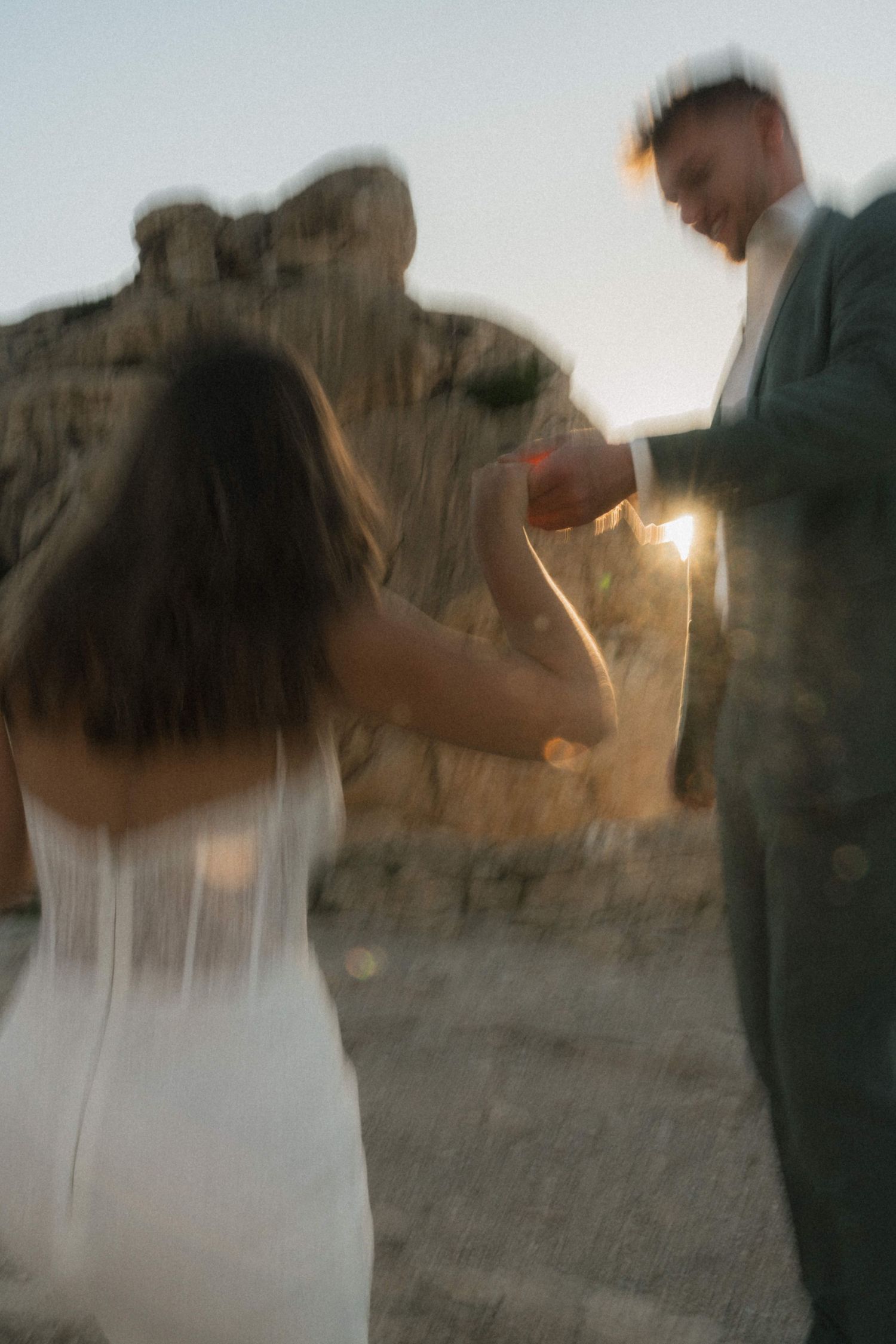 Blurred motion shot of a bride and groom holding hands at sunset near rocky landscape during outdoor wedding.