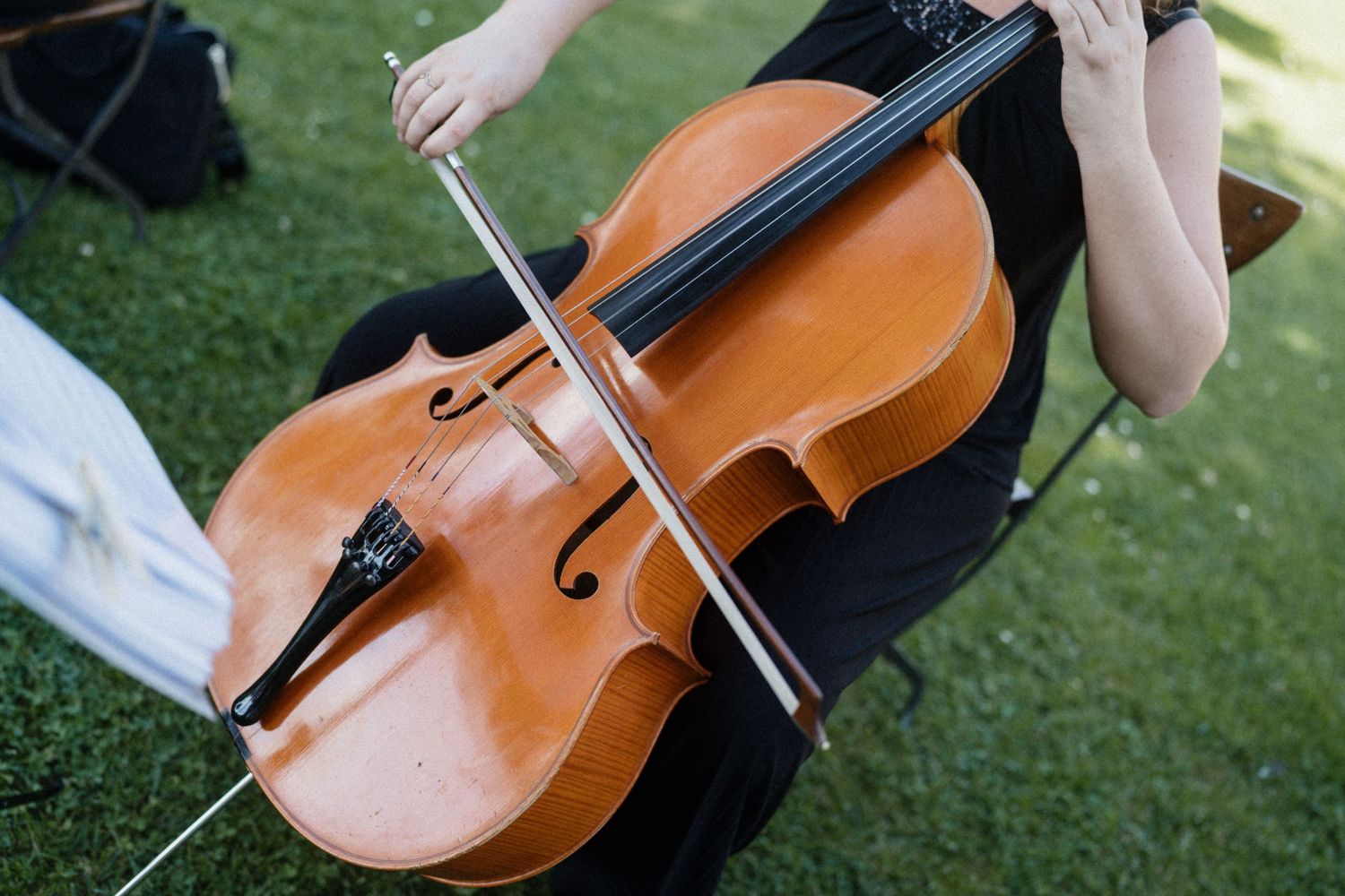 Close-up of a cellist playing during an outdoor wedding ceremony on a sunny day.