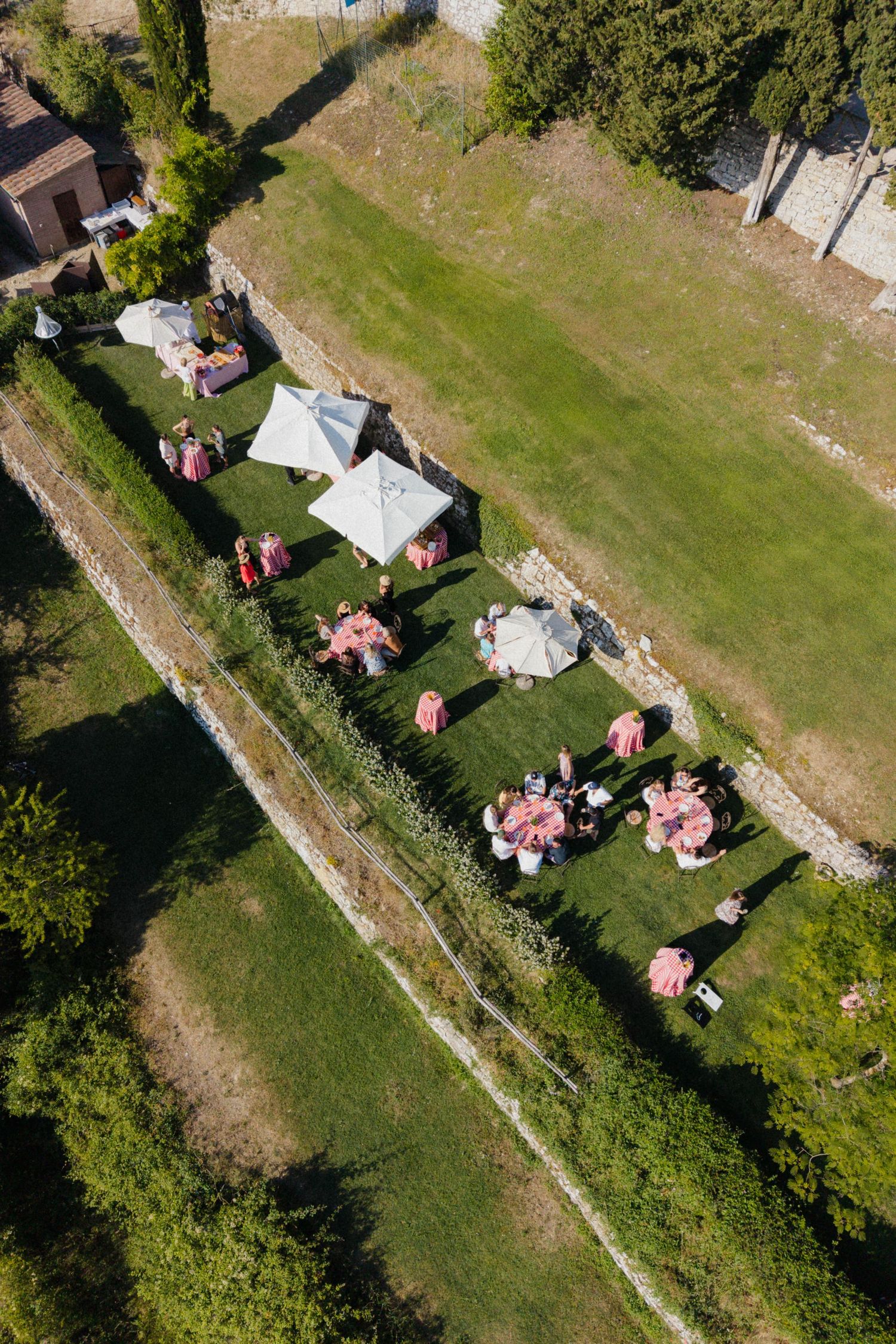 Aerial view of outdoor wedding reception with pink-themed tables and white umbrellas on green lawn.
