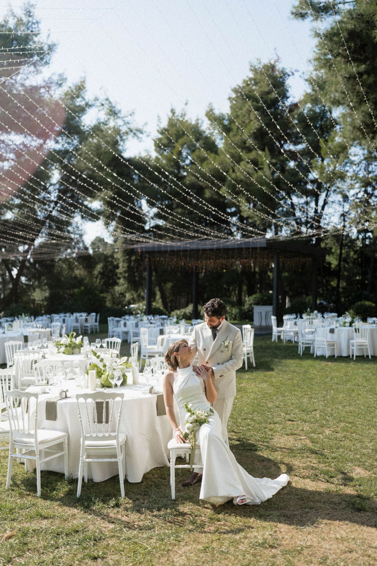 Bride and groom sharing a romantic moment at their elegant outdoor wedding reception with white tables and string lights.