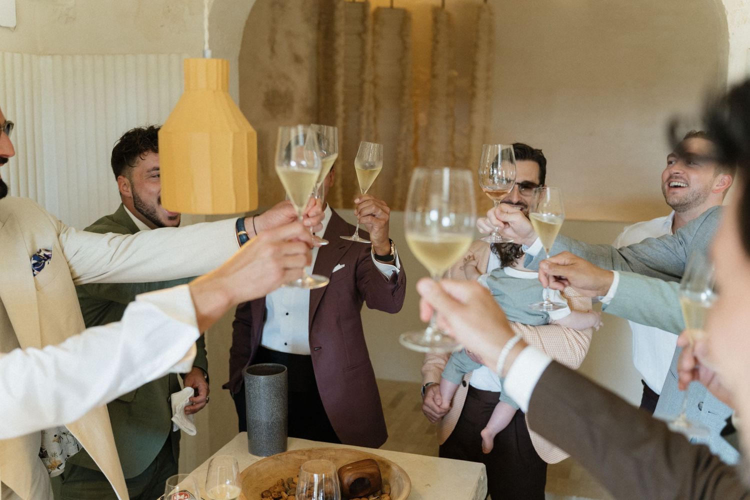 Group of men in suits raising champagne glasses together for a celebratory toast around a table in a warmly lit room.
