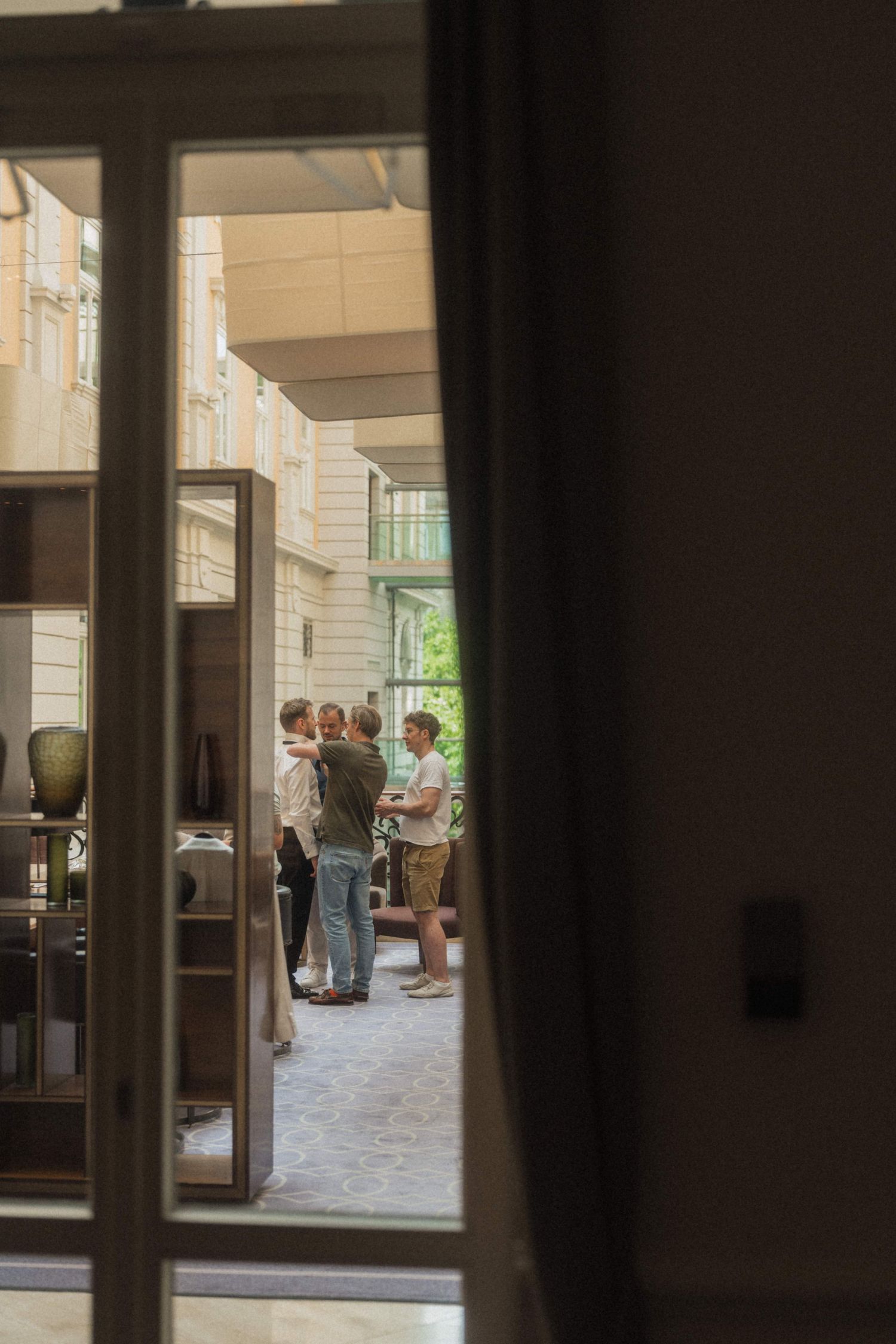 People socializing in a sunlit courtyard viewed through an open doorway of an elegant building.