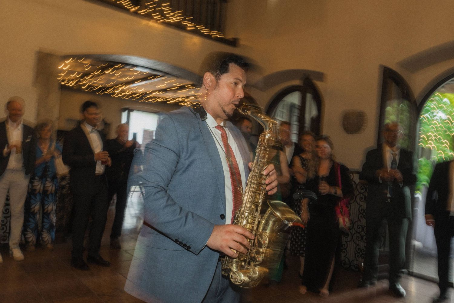Saxophonist in blue suit performing live music for wedding reception guests indoors.