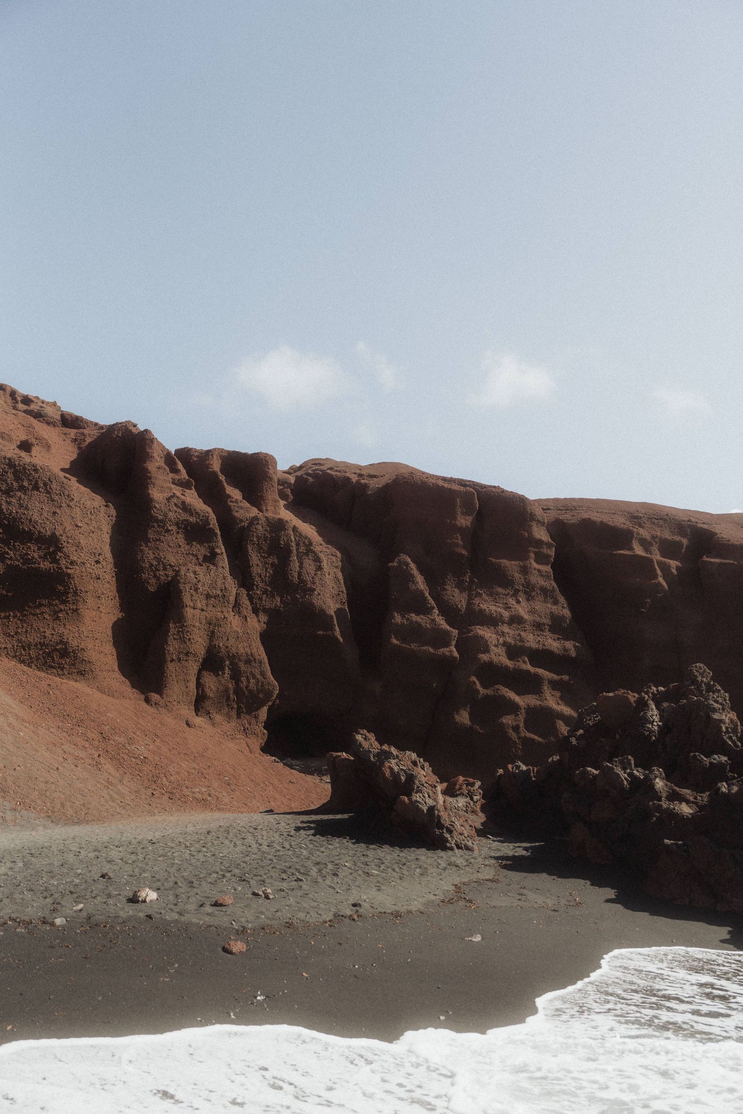 Red volcanic cliffs and black sand beach with ocean waves in Santorini, Greece.