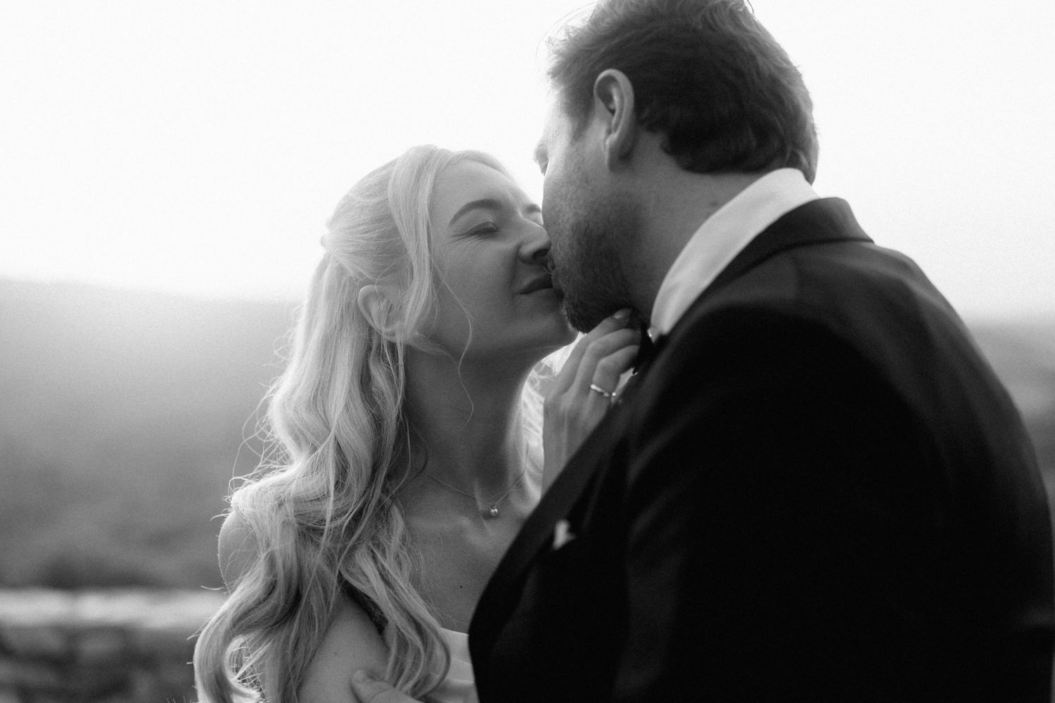 Black and white close-up of a bride and groom sharing a tender kiss at sunset.