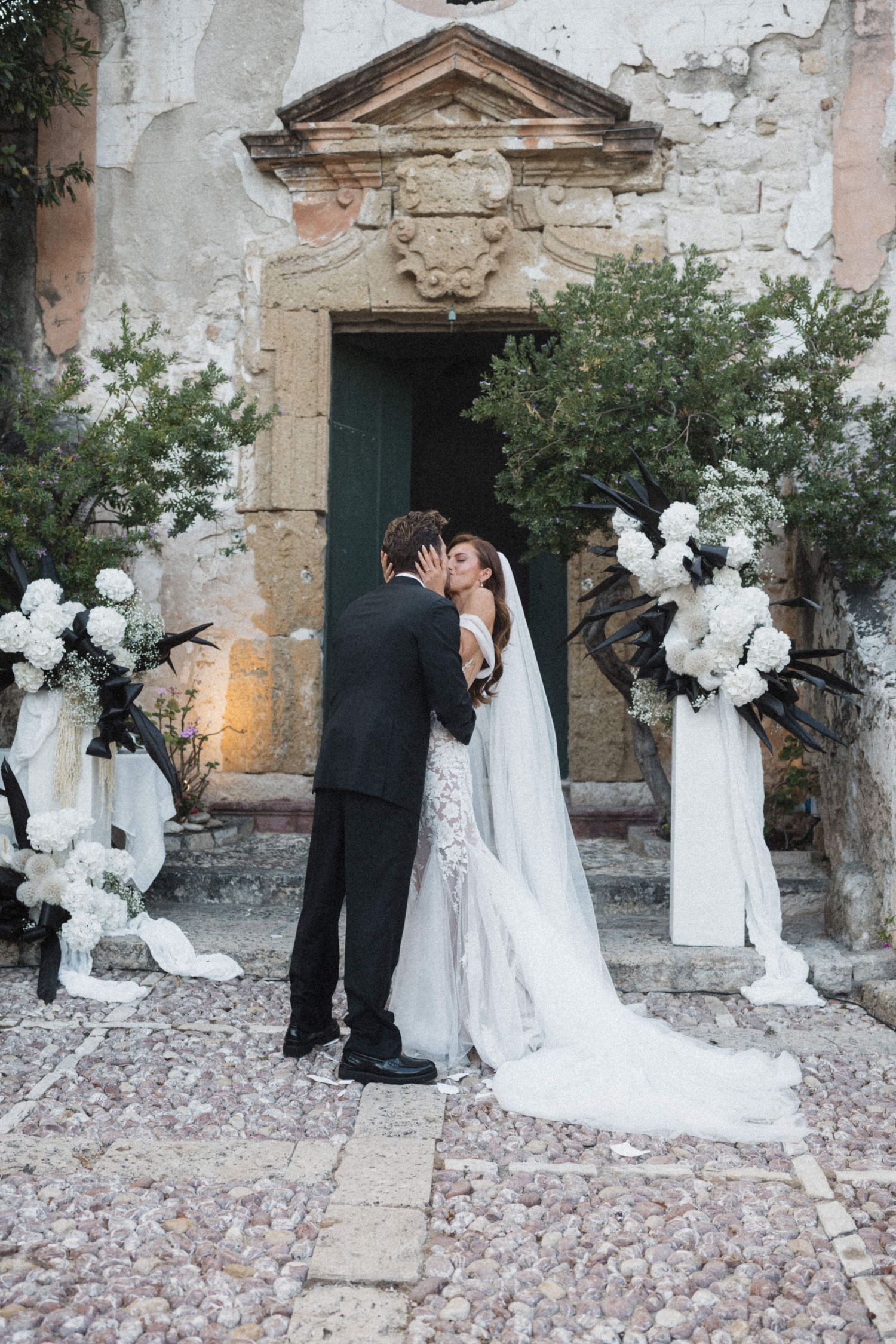 Bride and groom share first kiss at altar decorated with white floral arrangements.